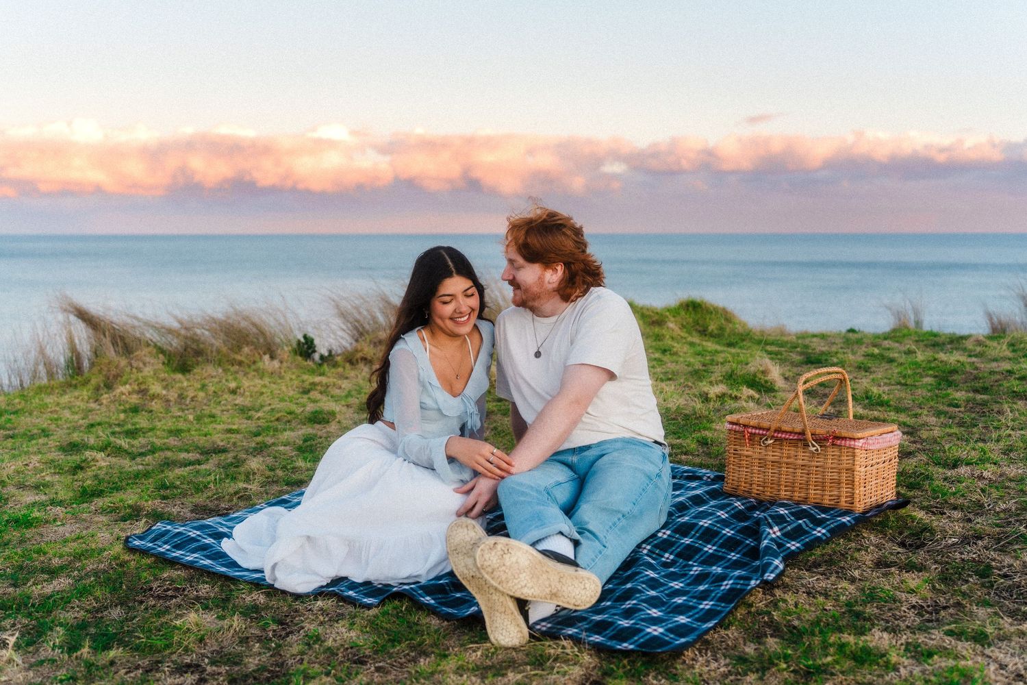 A couple enjoys a romantic picnic by the ocean at sunset.