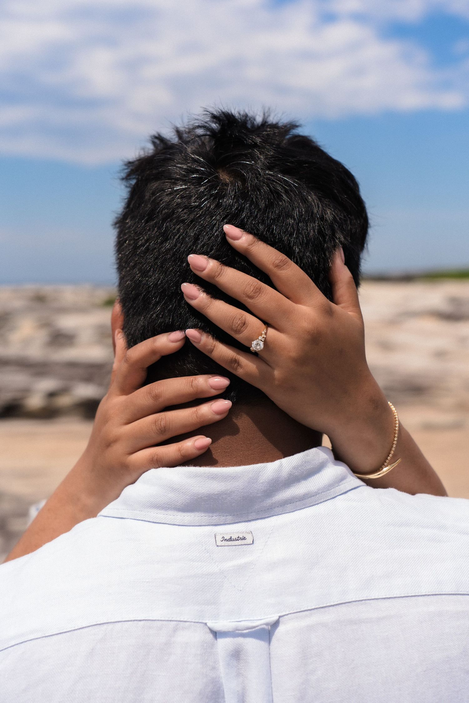 Close-up of hands touching the back of a white shirt against coastal background.