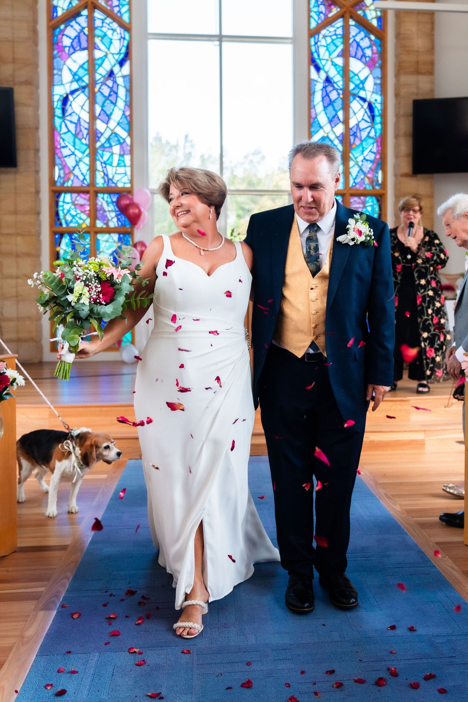 Wedding couple walking down aisle with rose petals scattered on blue carpet.