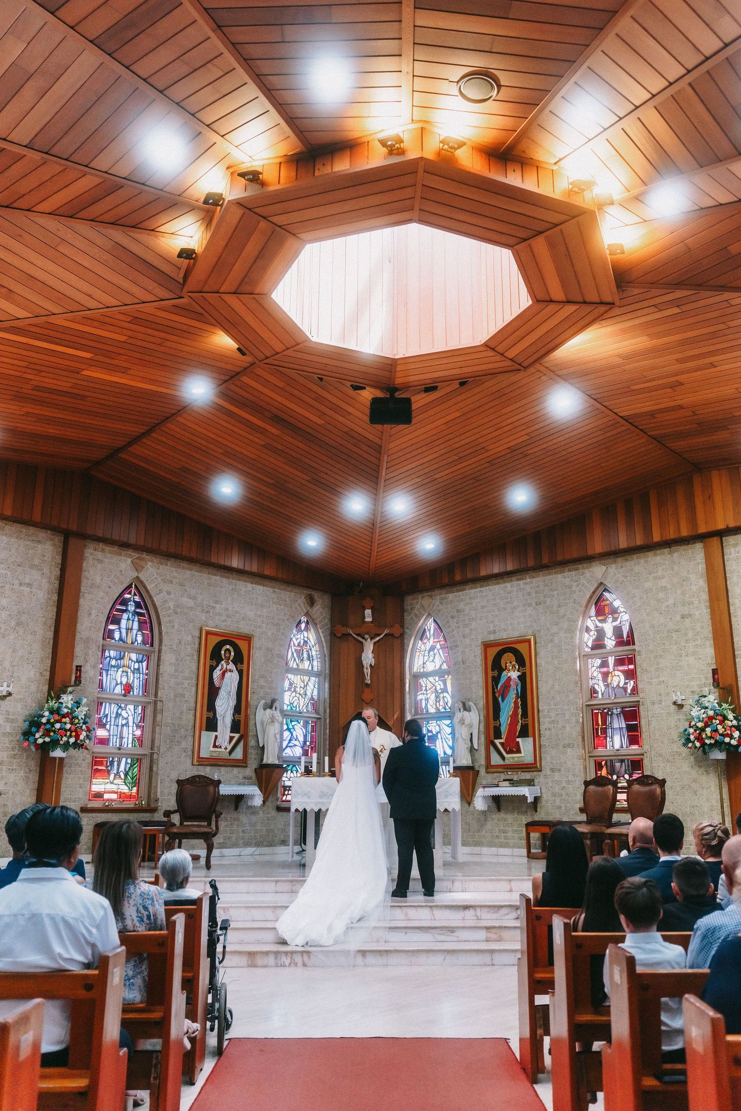 Church interior with wooden ceiling and stained glass windows during wedding ceremony.