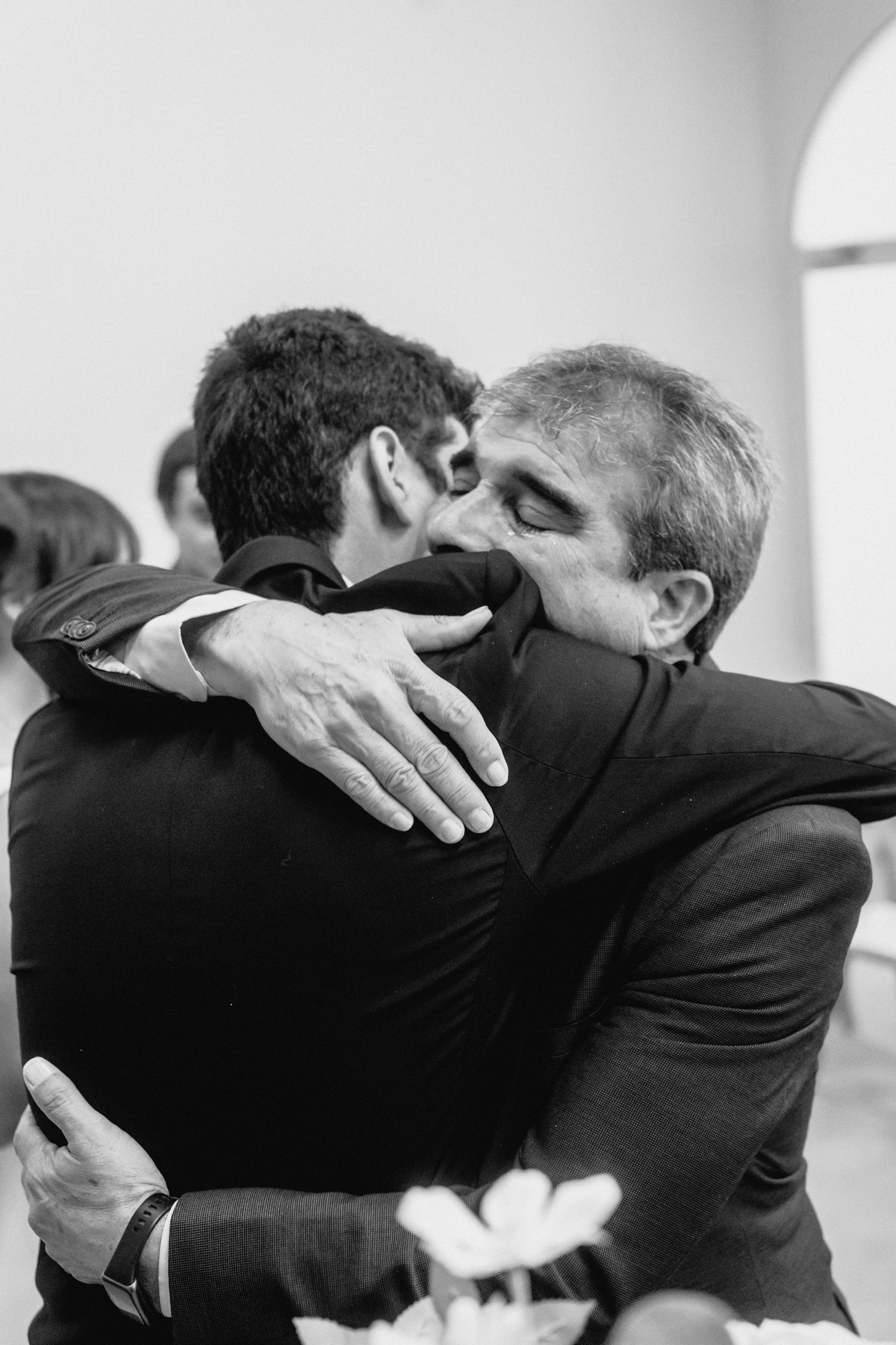 A series of emotional embraces between wedding guests shown in black and white.