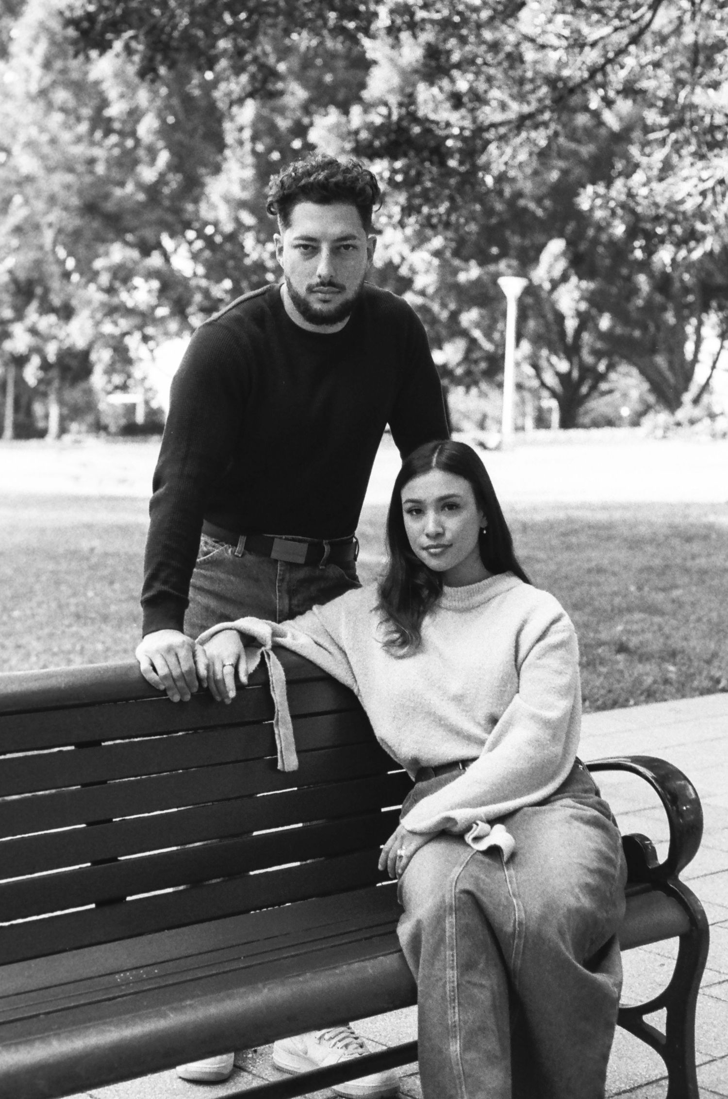 A couple poses together on a park bench in black and white photography.