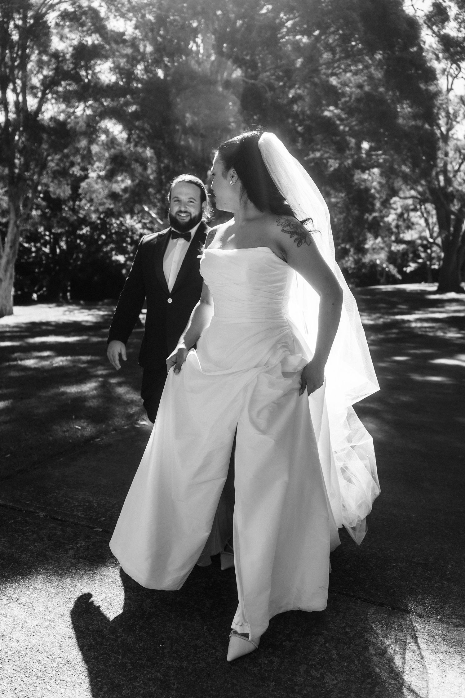 Black and white photo of playful dancing figures in formal attire casting shadows outdoors.