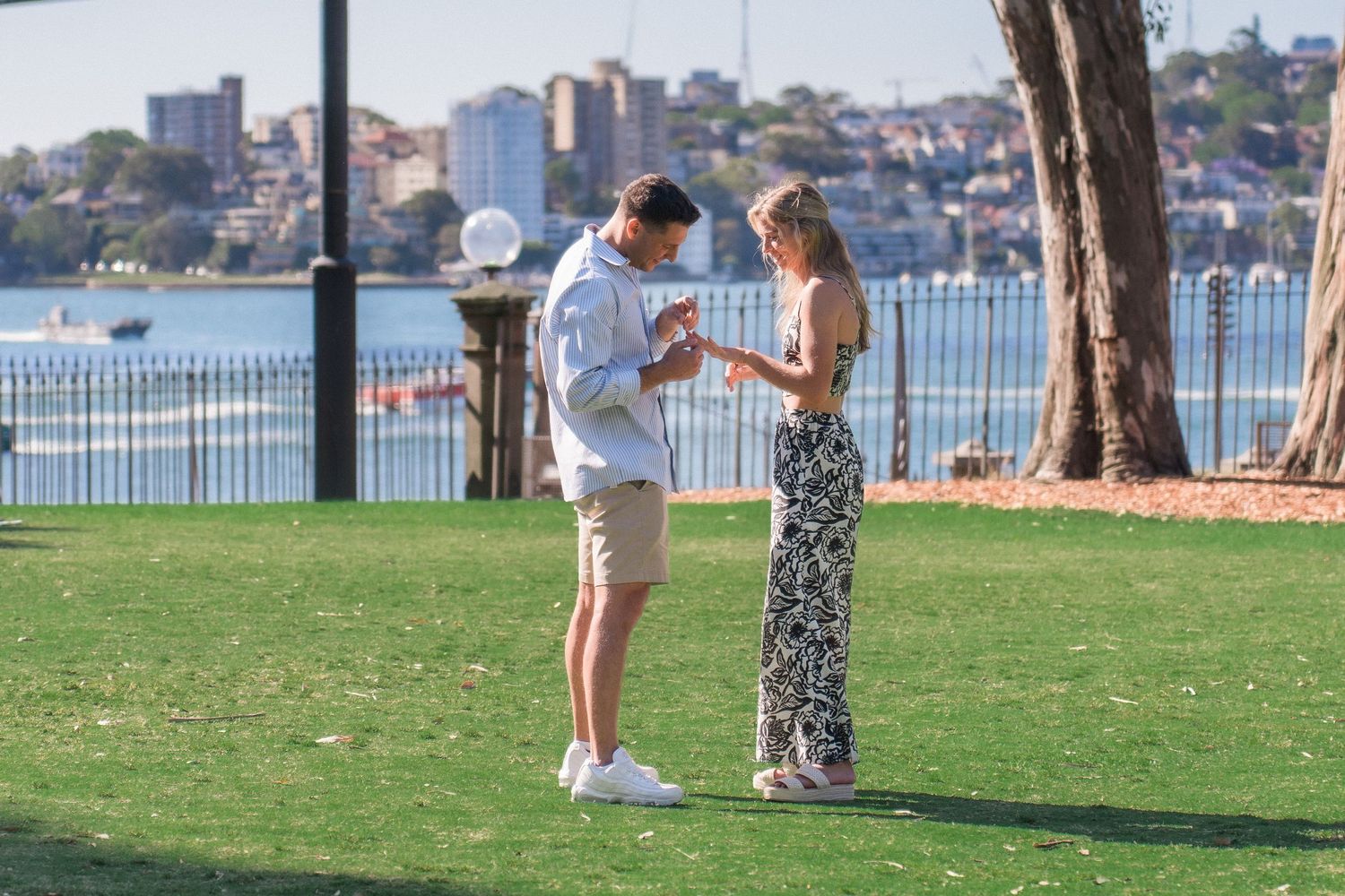 A romantic proposal unfolds on grassy area near Sydney Opera House.