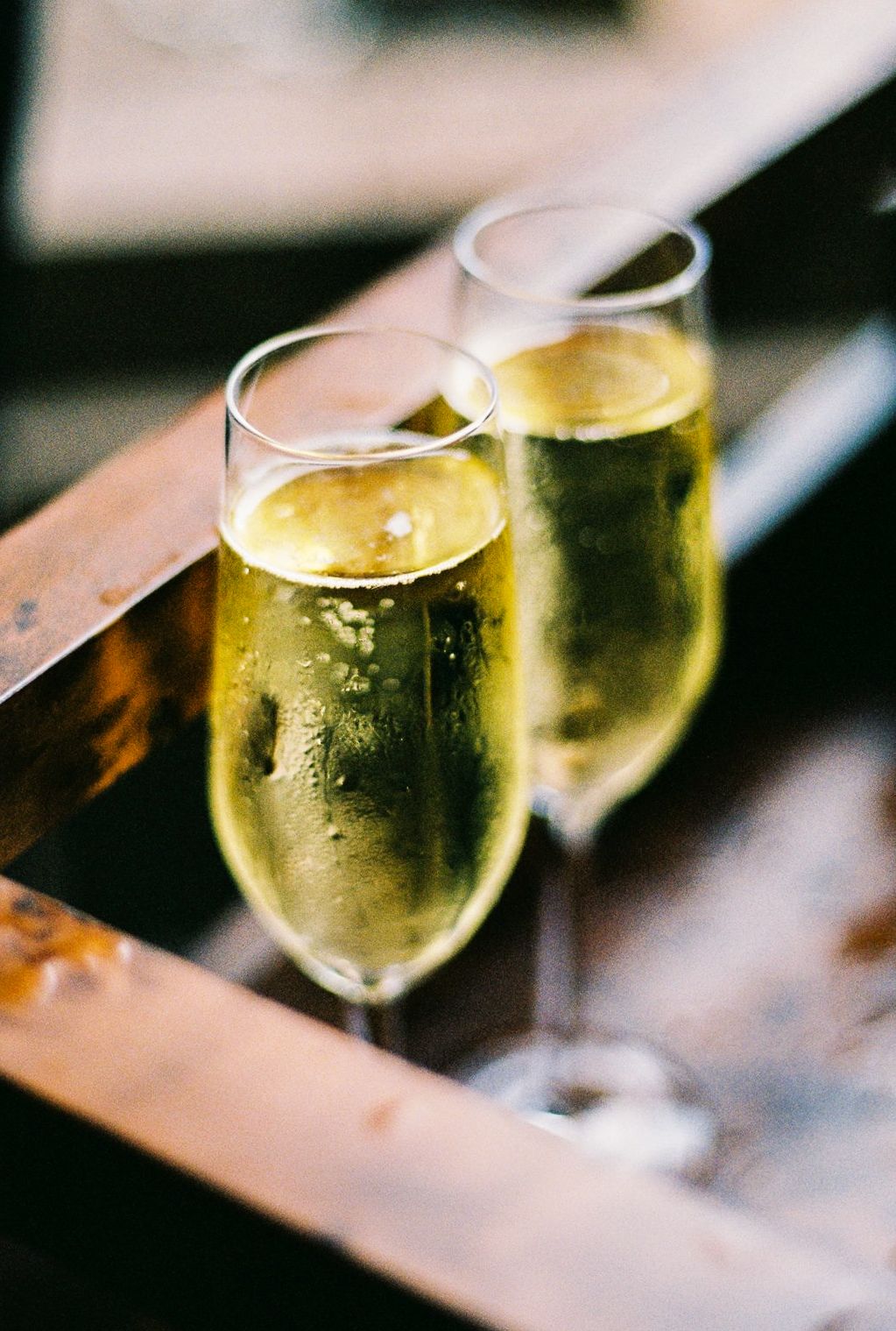 Two elegant champagne flutes filled with sparkling wine on a rustic wooden tray.