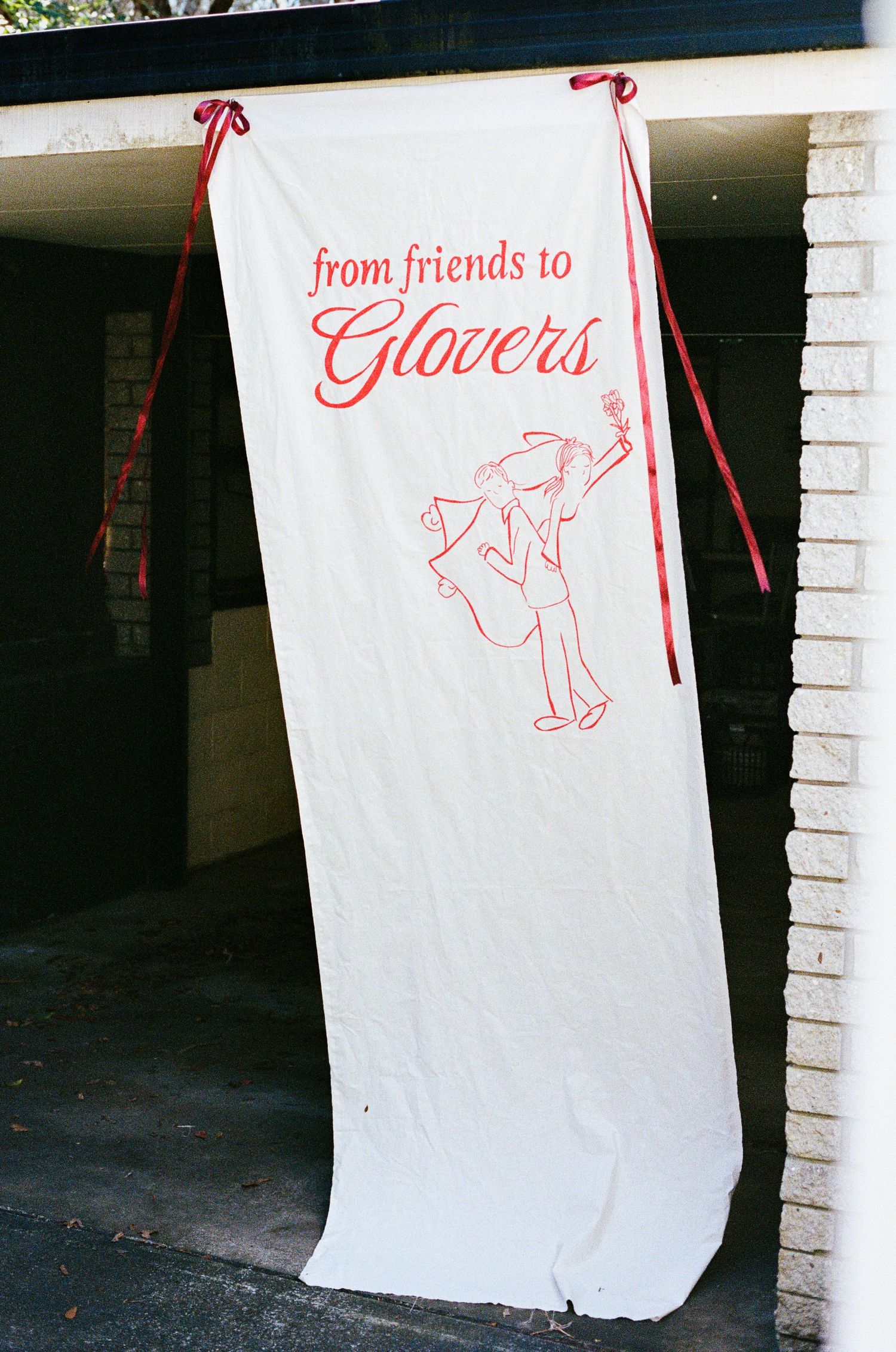 White banner with red text reading 'from friends to Glovers' with illustration hanging on brick wall.