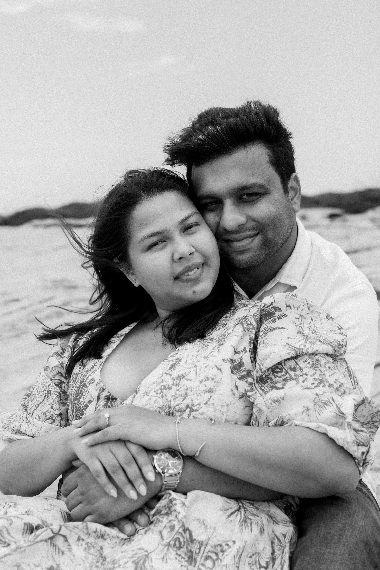 Black and white photo of an embrace on a windy coastal day.