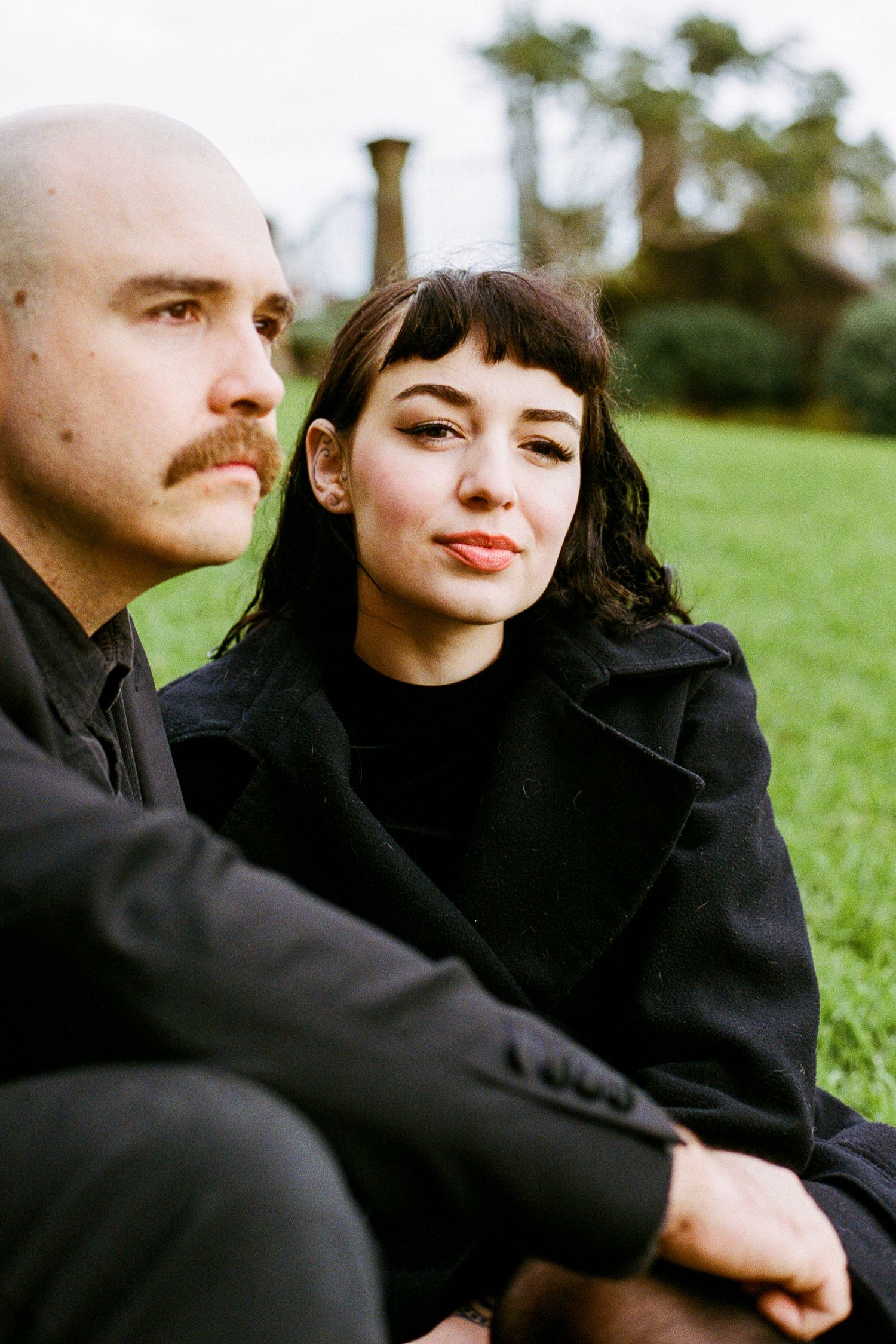 A couple in matching black outfits shares tender moments while sitting together outdoors.