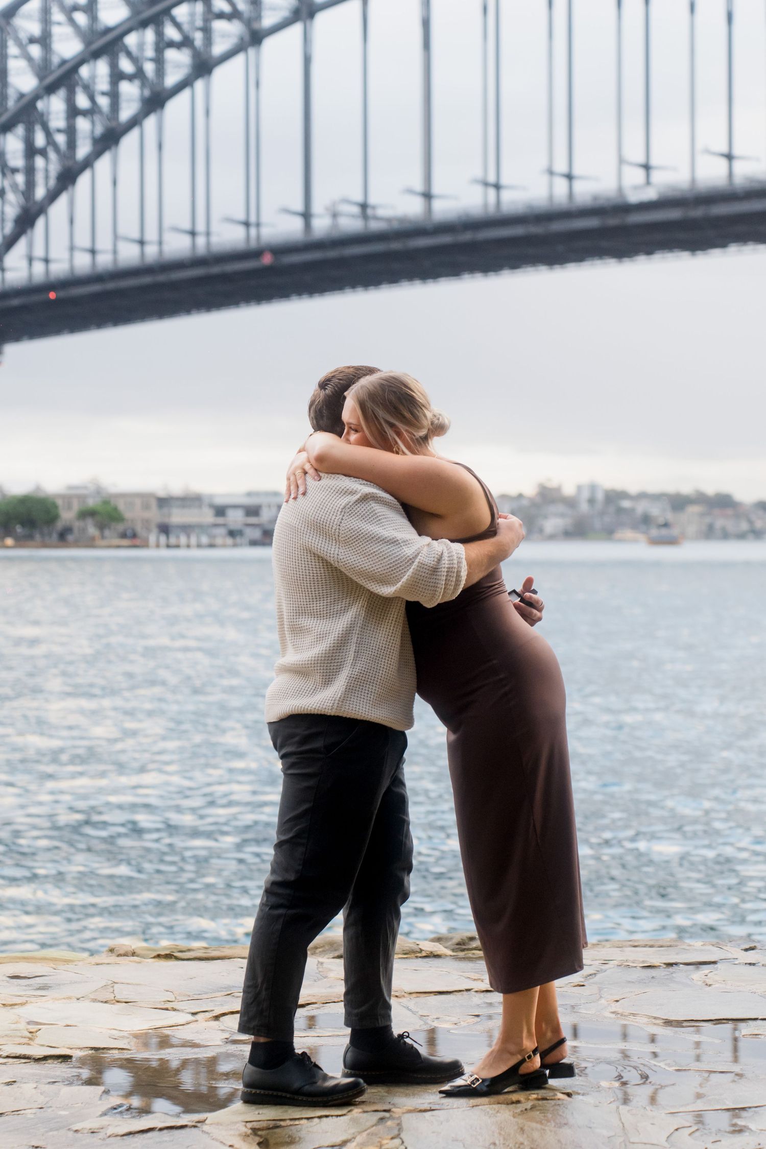 A tender moment shared between a couple by the harbour with the bridge overhead.