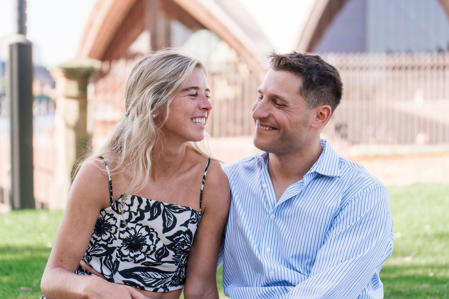 A couple shares a romantic moment on grass with Sydney Harbour landmarks in the background.