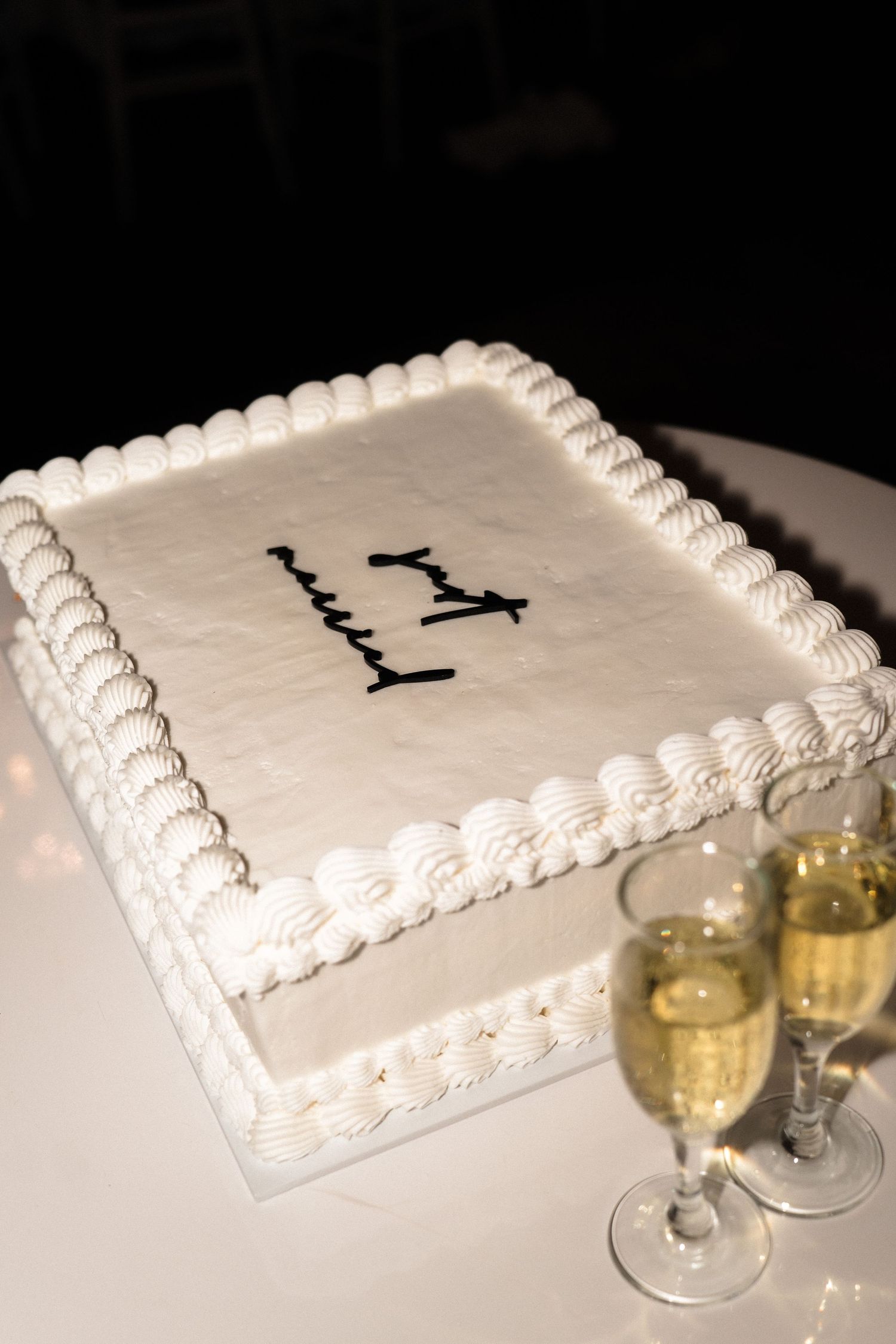 Simple white square wedding cake with piped border and champagne flutes.