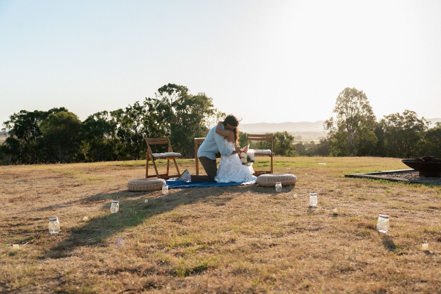 A couple sharing a romantic picnic on a hilltop with candles at sunset.