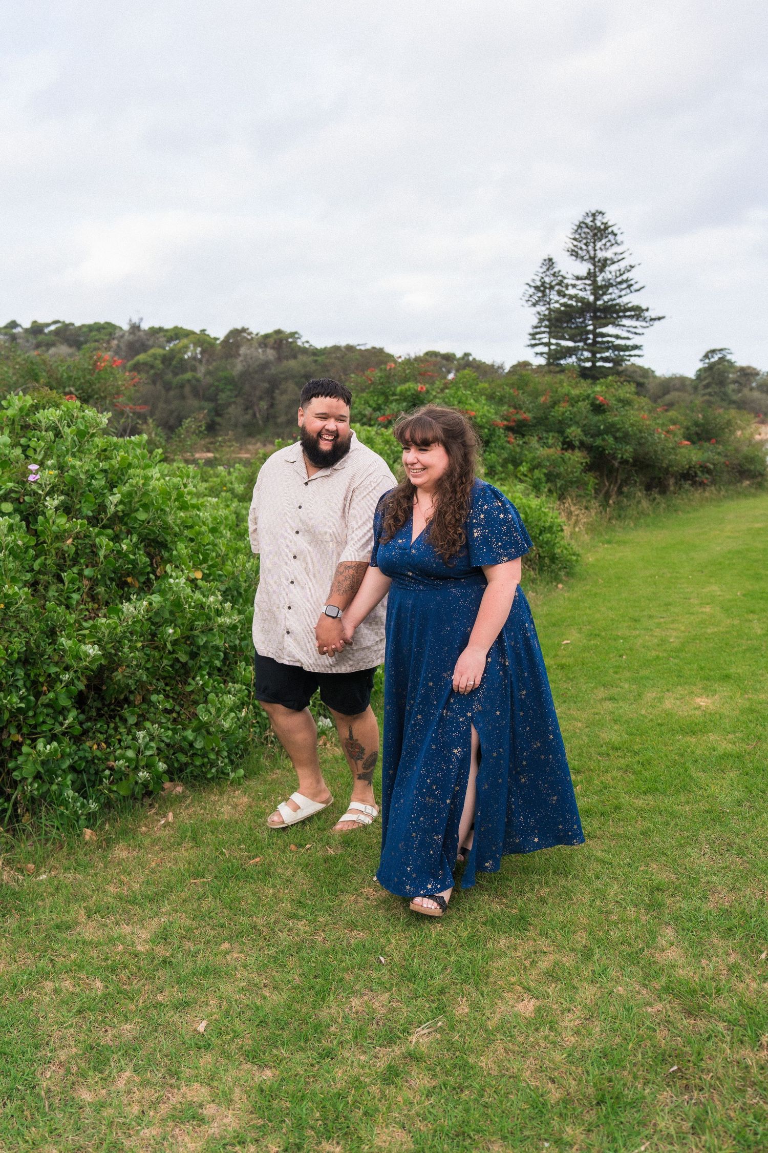 Couple walking together on a grassy coastal hillside wearing coordinated blue and beige outfits.