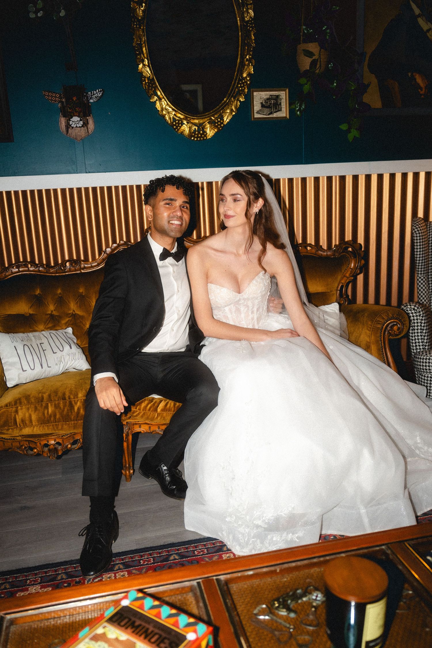 Newlyweds share a moment on an ornate gold couch in a luxuriously decorated room.