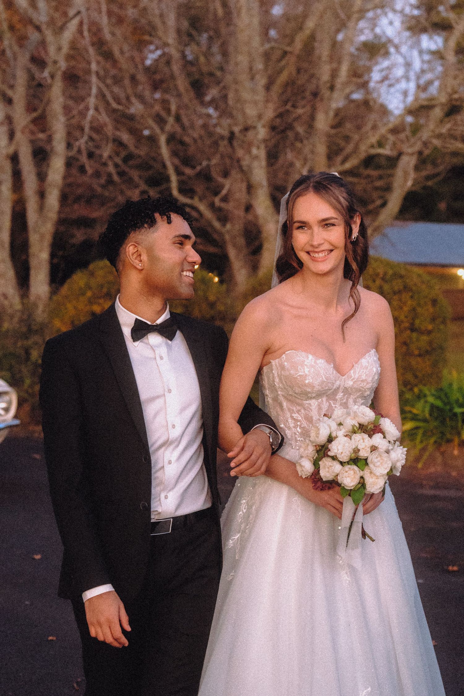 Newlyweds share joyful moments with white bouquet against autumn trees.