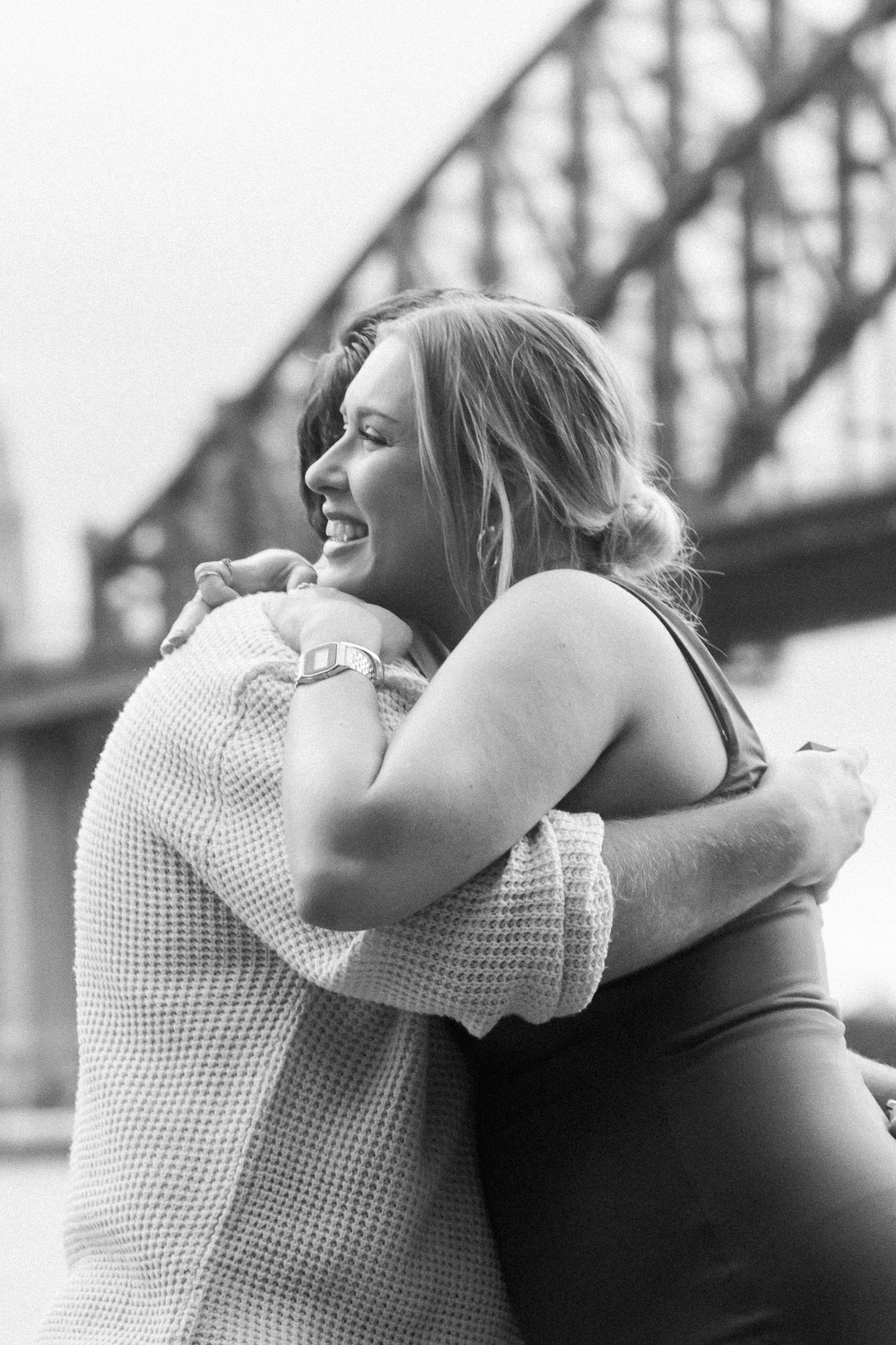 An emotional embrace captured in black and white with the bridge silhouette visible behind.