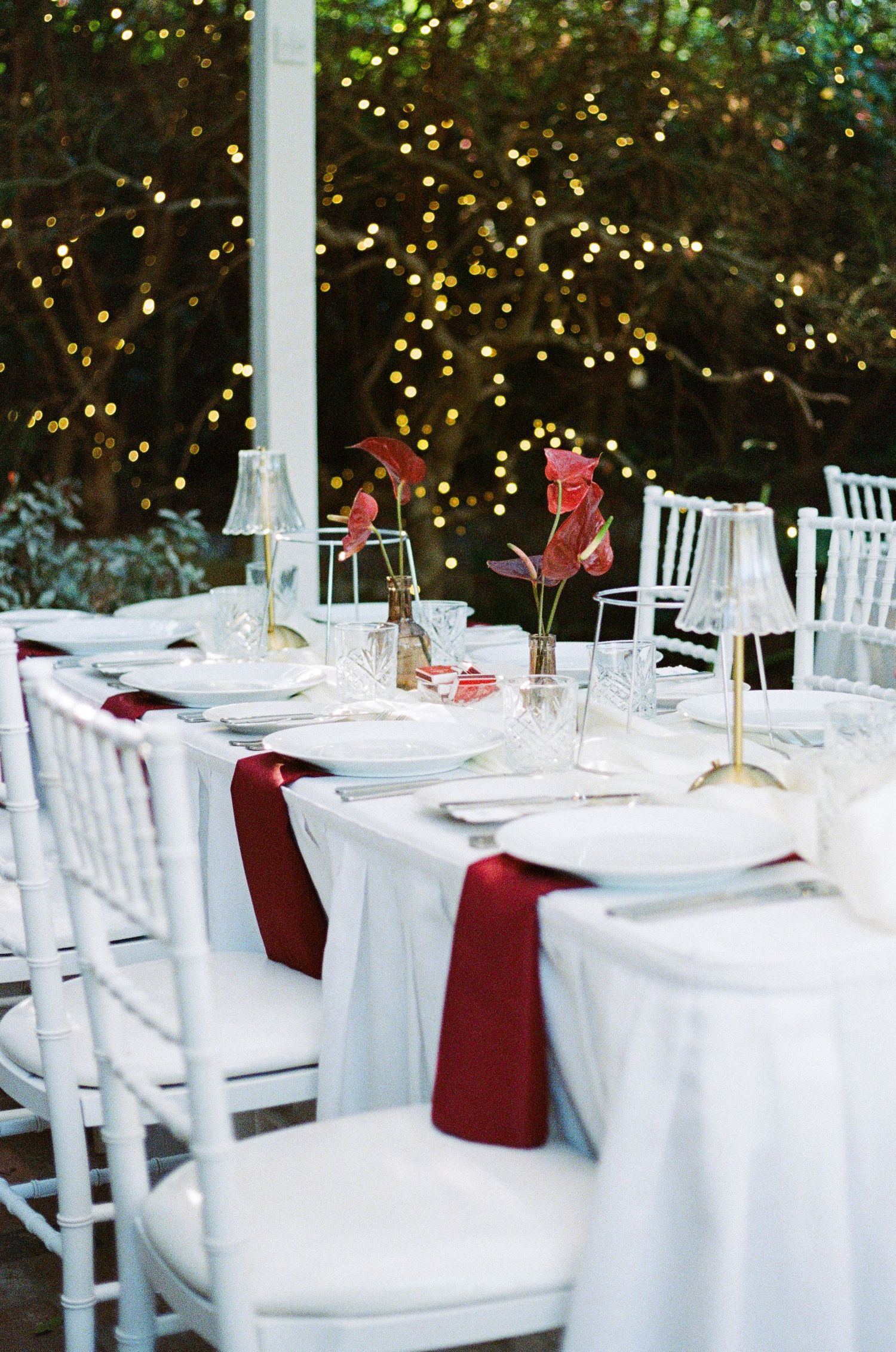 Elegant wedding reception table setting with white linens and burgundy accents.