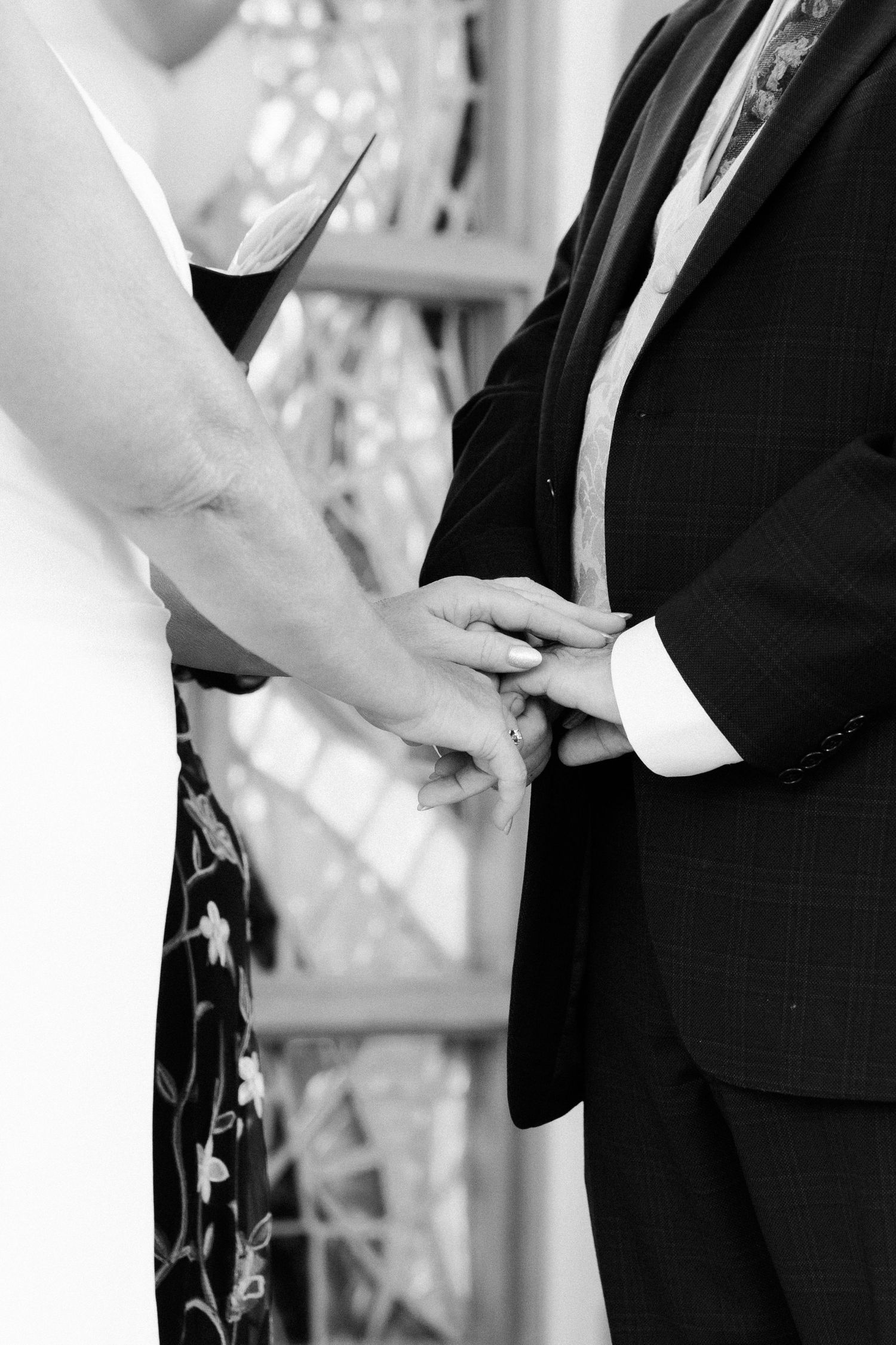 Close-up black and white shot of hands exchanging rings during a wedding ceremony.