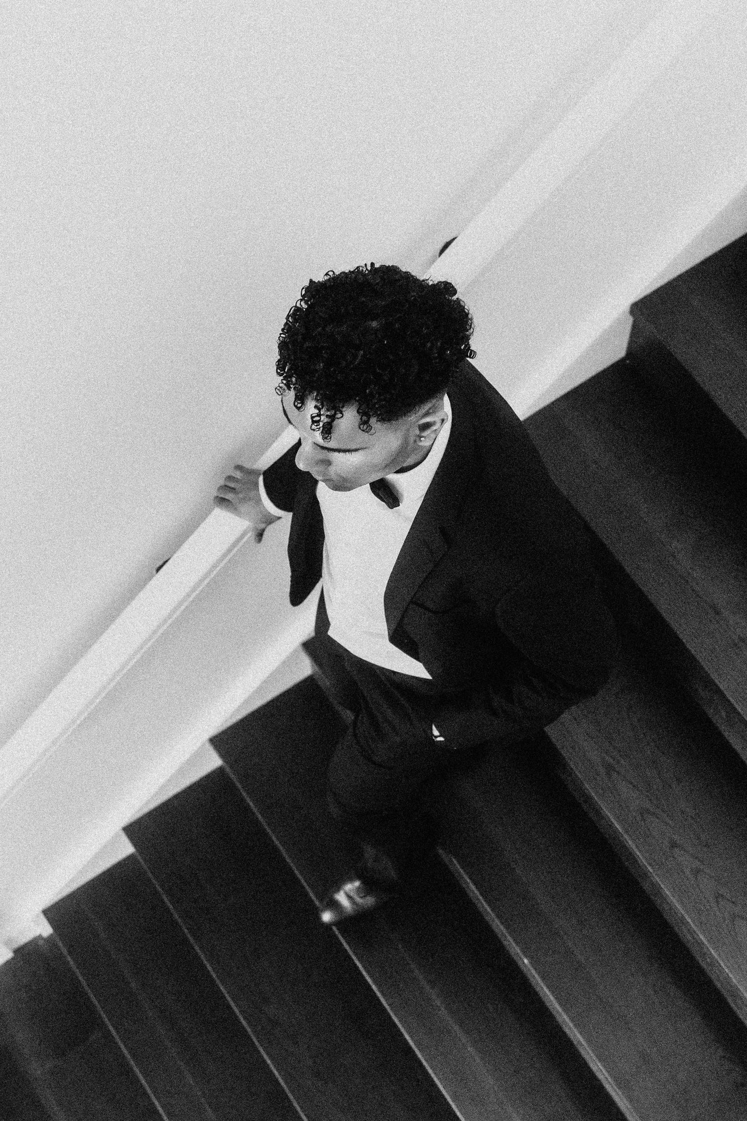 Artistic black and white portrait of man in formal wear on staircase.
