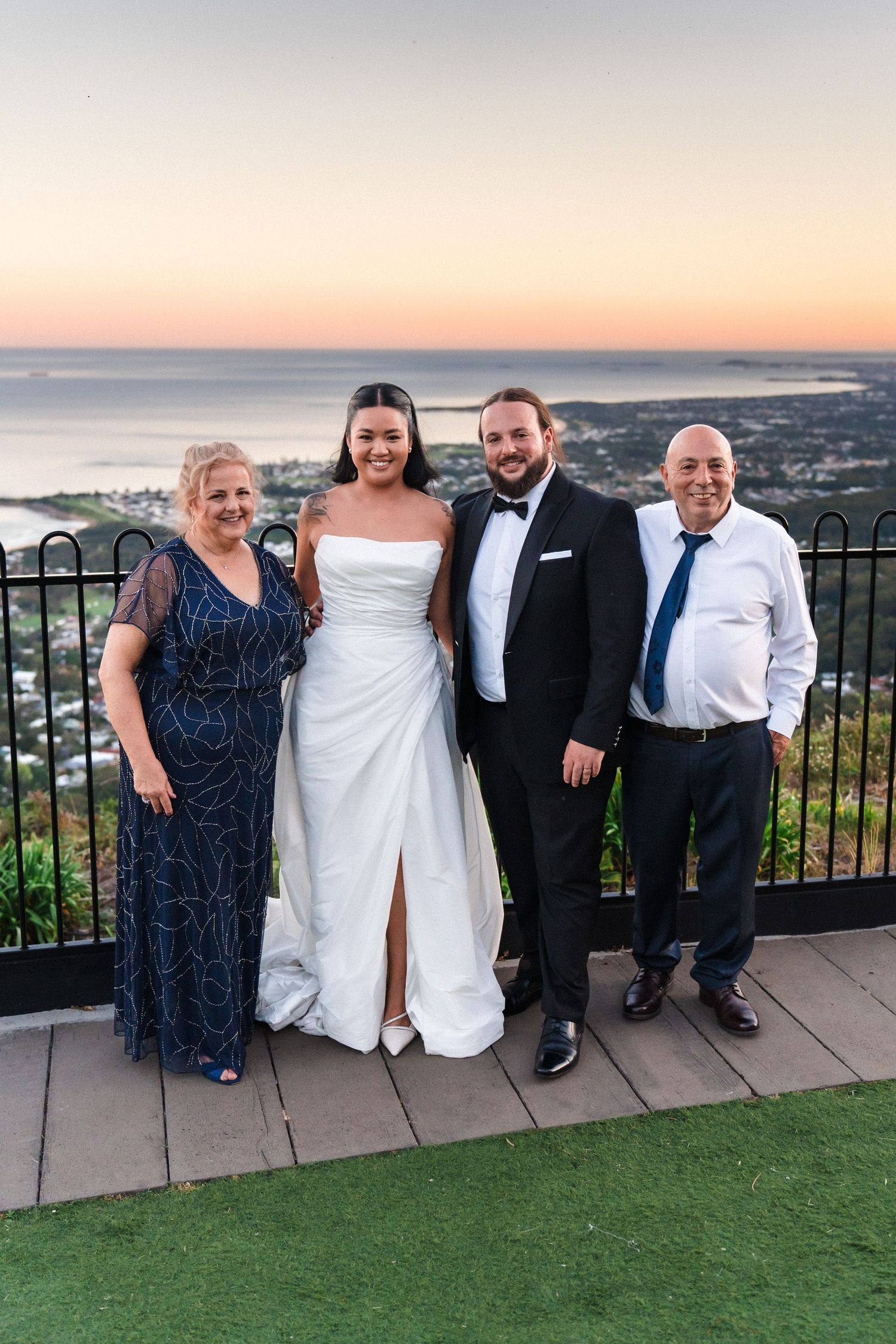 Wedding party poses at sunset on scenic overlook with ocean view in background.