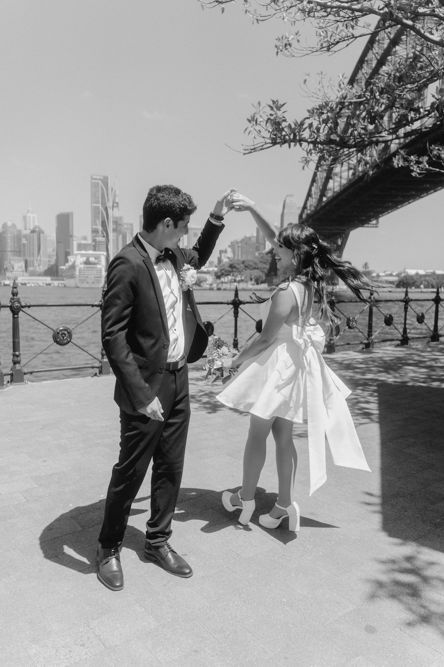 Black and white photos of a couple dancing together under a tree with a city skyline.