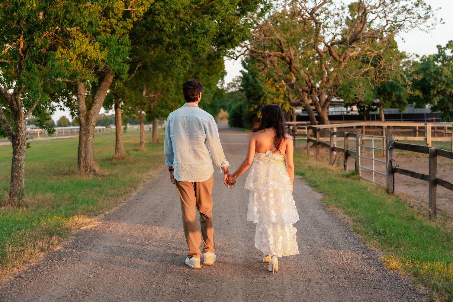 A couple walks hand in hand down a tree-lined path at sunset creating a romantic silhouette.