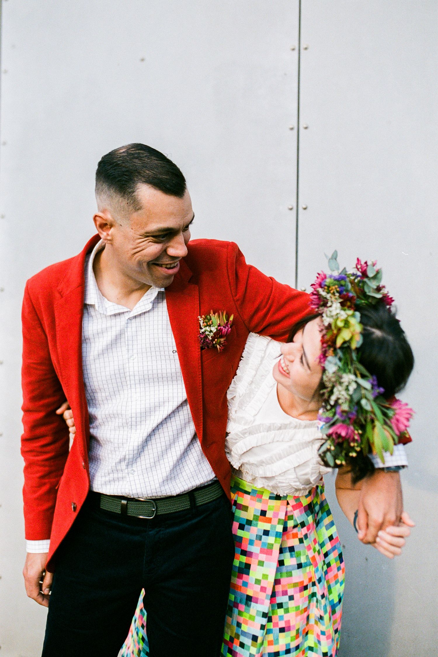 Couple in red jacket and colorful dress sharing a candid laughing moment.