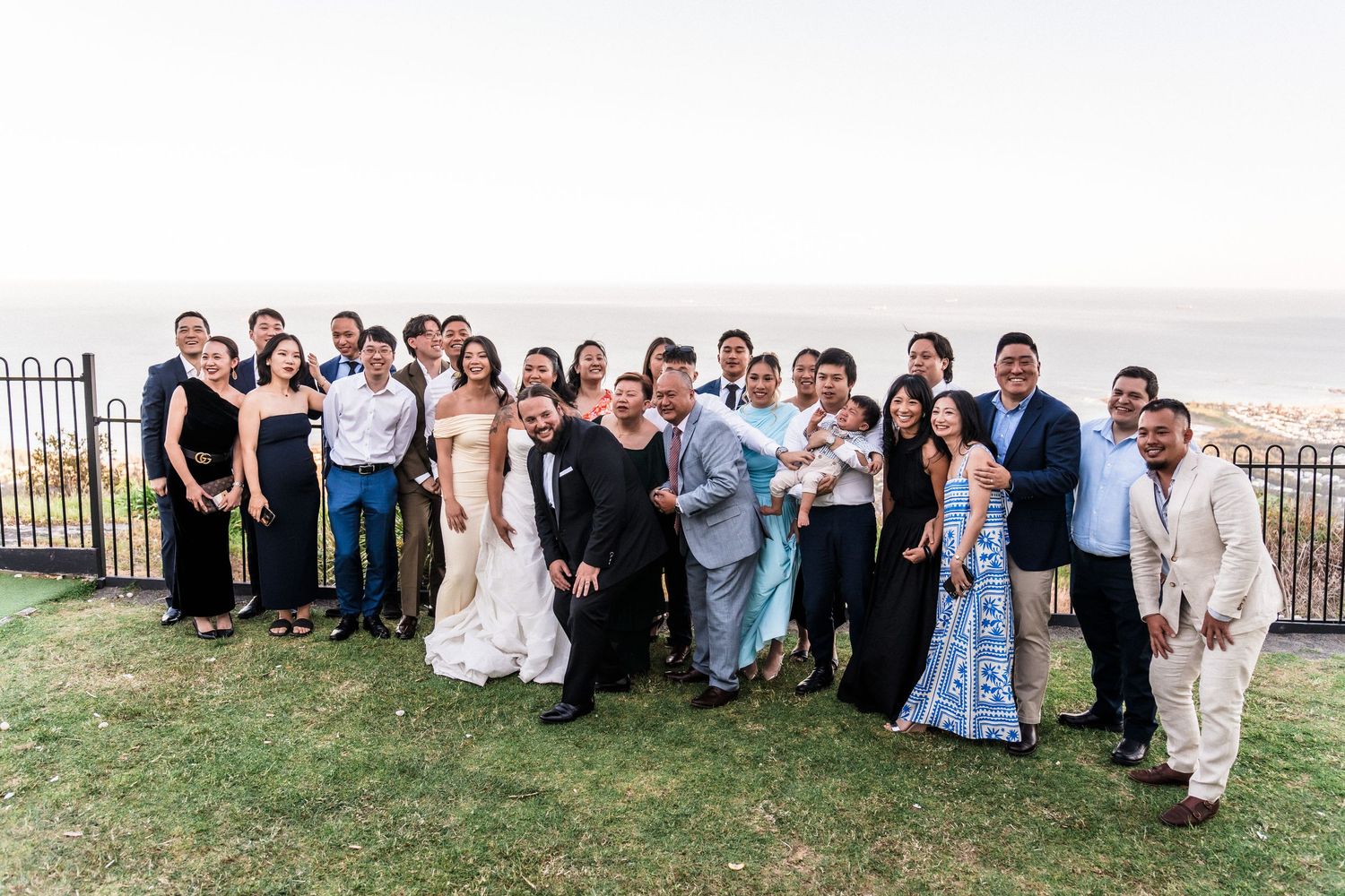 Large group photo of wedding guests gathered outdoors on grassy hillside.