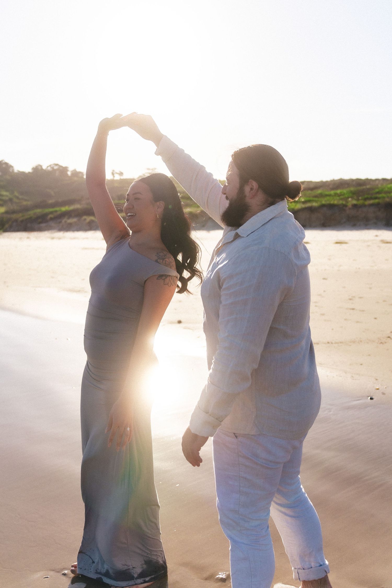 A couple dances playfully on the beach during golden hour.
