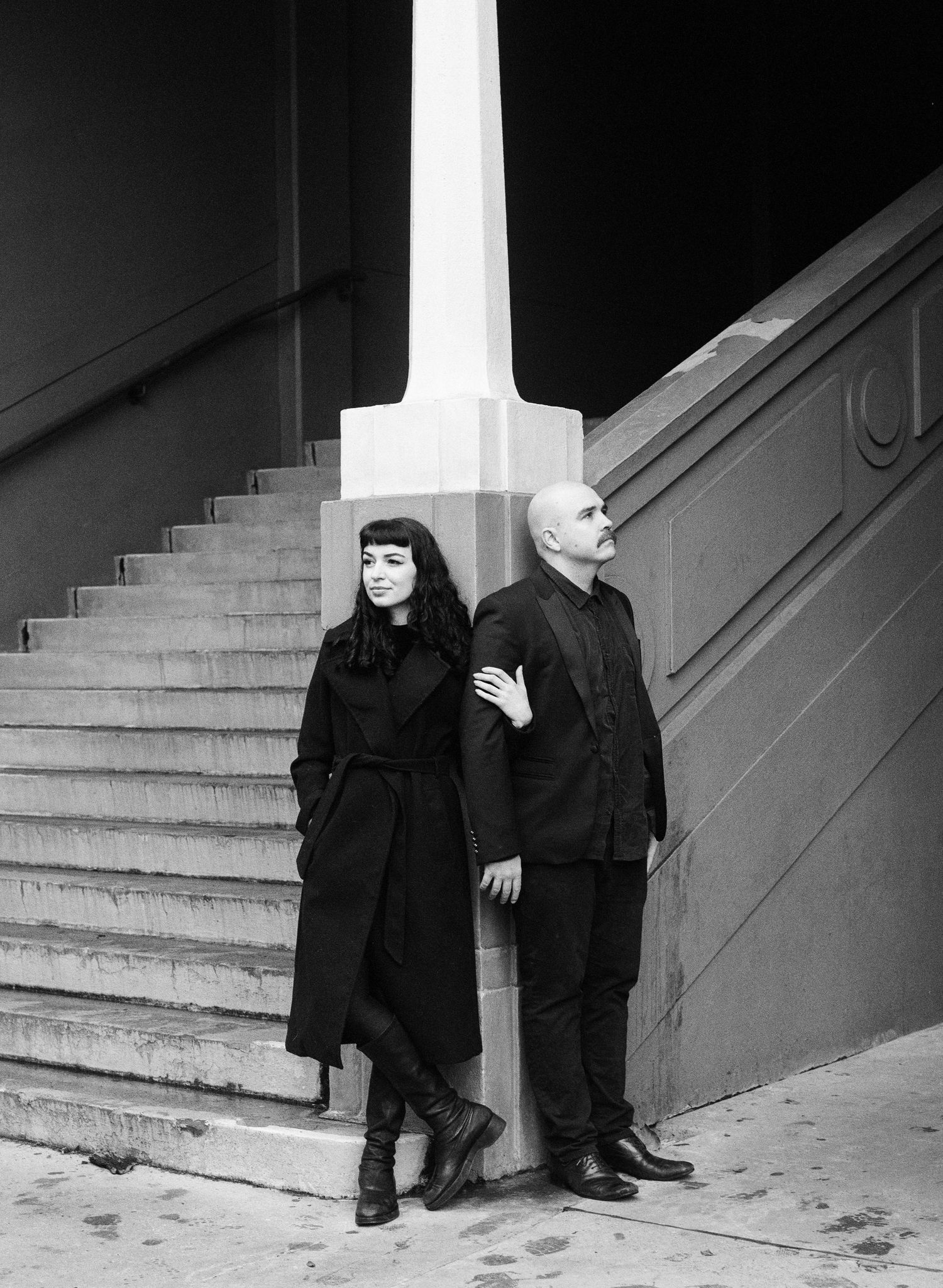 Two figures in dark clothing pose playfully on concrete steps.