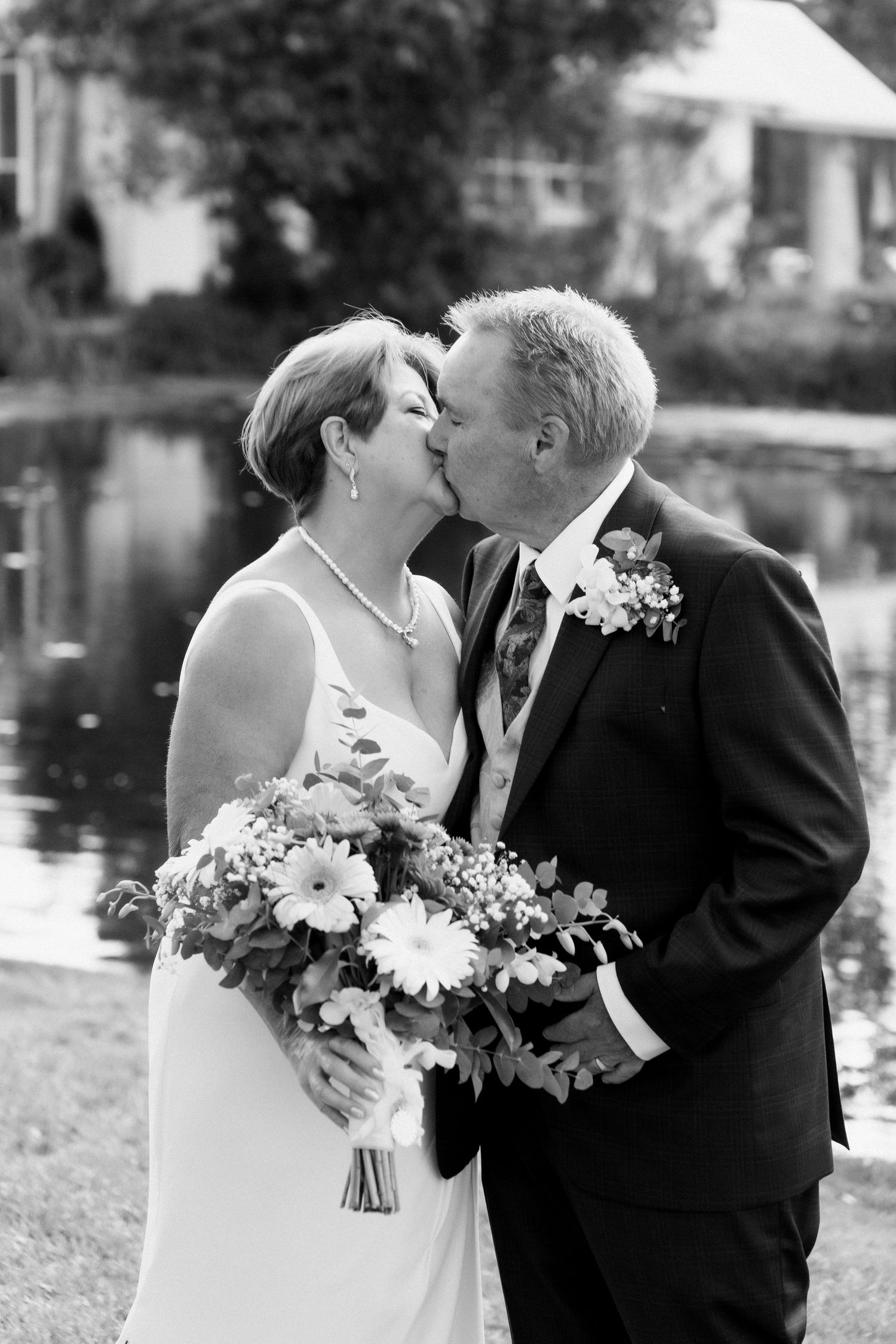 A series of romantic wedding photos showing tender kisses between a couple by a lake with white flowers.