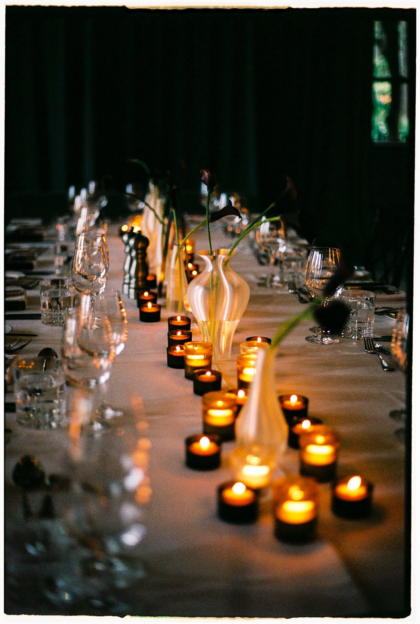 Elegant candlelit dining table with glowing tea lights, white vases, and crystal glassware for a romantic event.