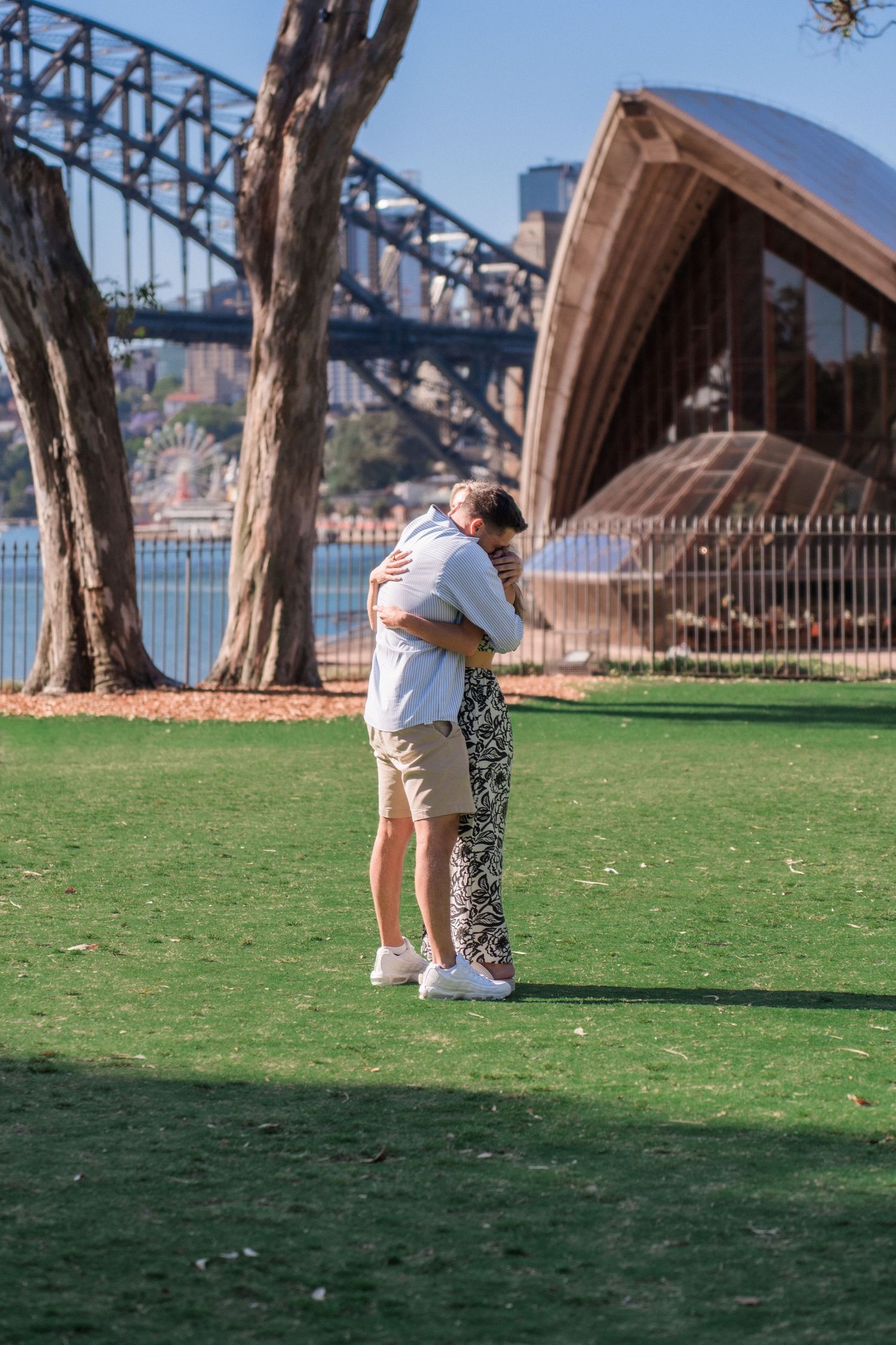 A couple shares a special moment on grass with Sydney Opera House and Harbour Bridge in background.