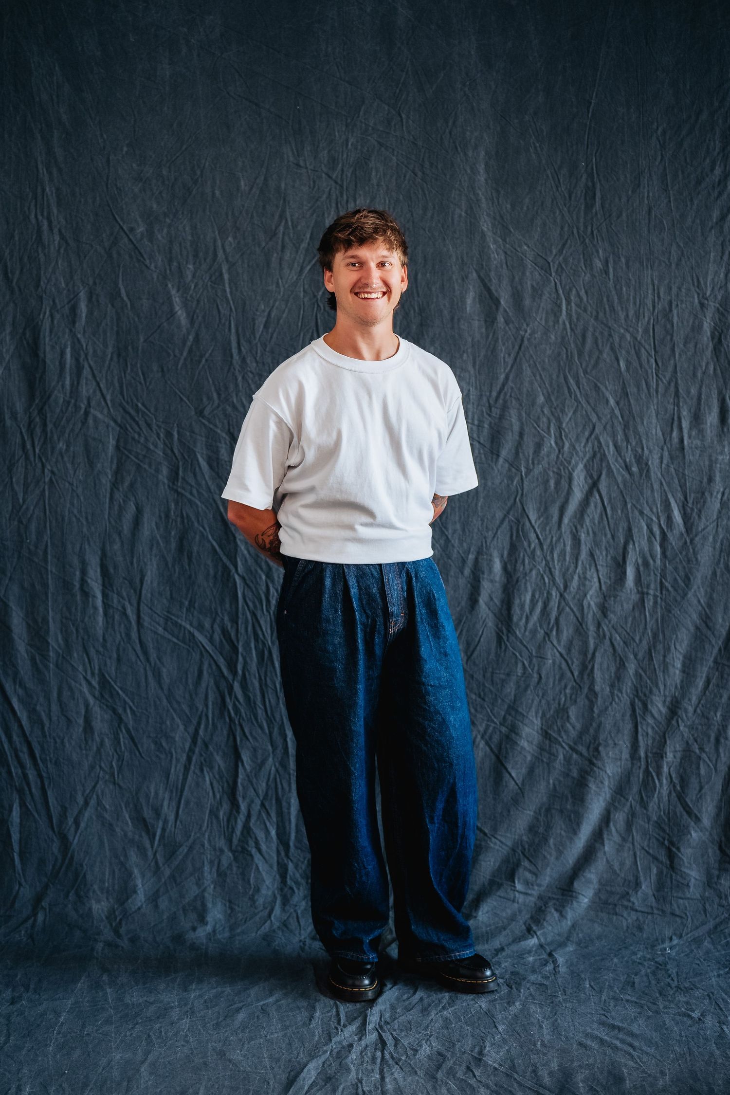 Studio portrait against dark backdrop showing relaxed casual style with white tee and navy pants.