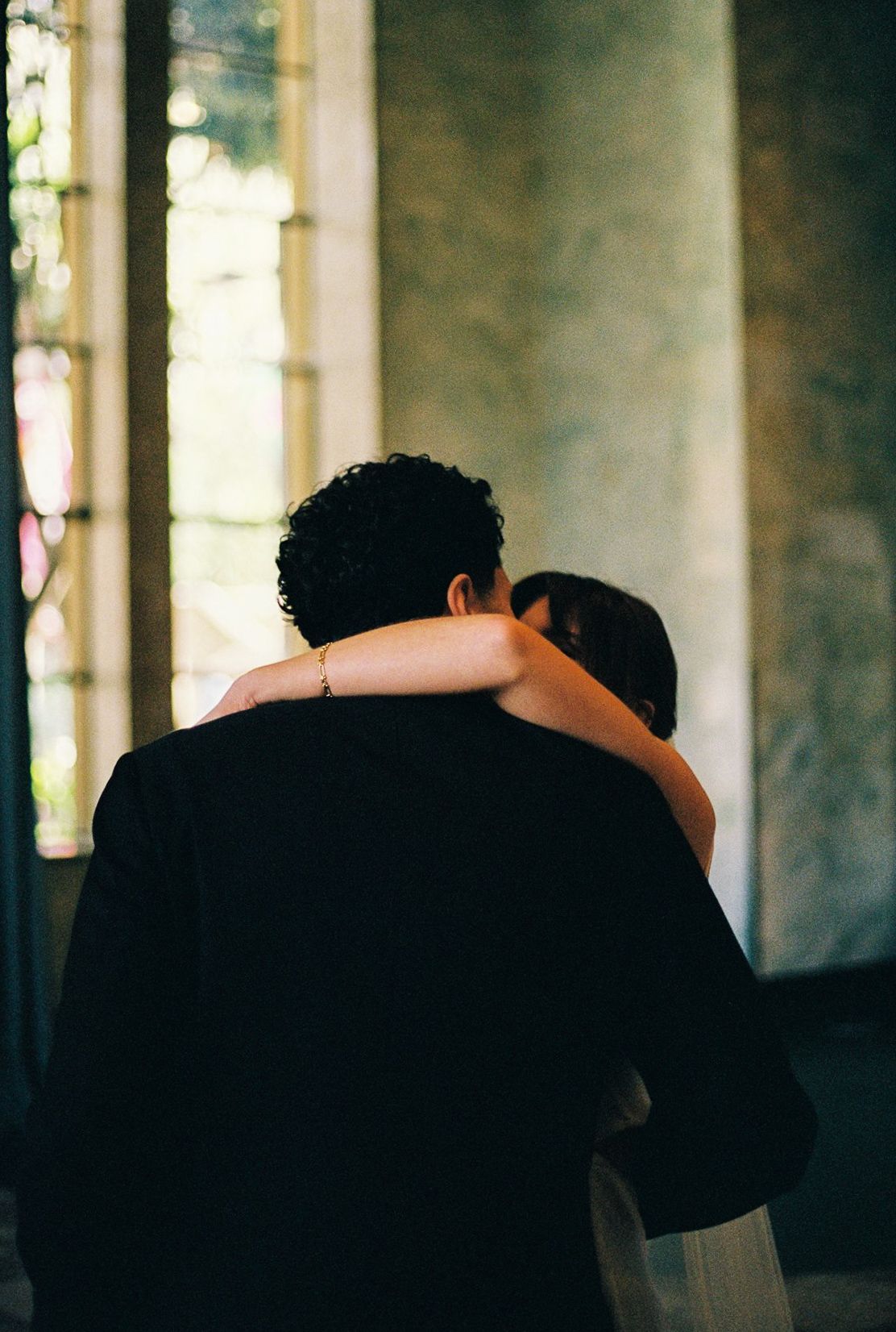 Newlyweds sharing tender embrace near stained glass windows after wedding ceremony.