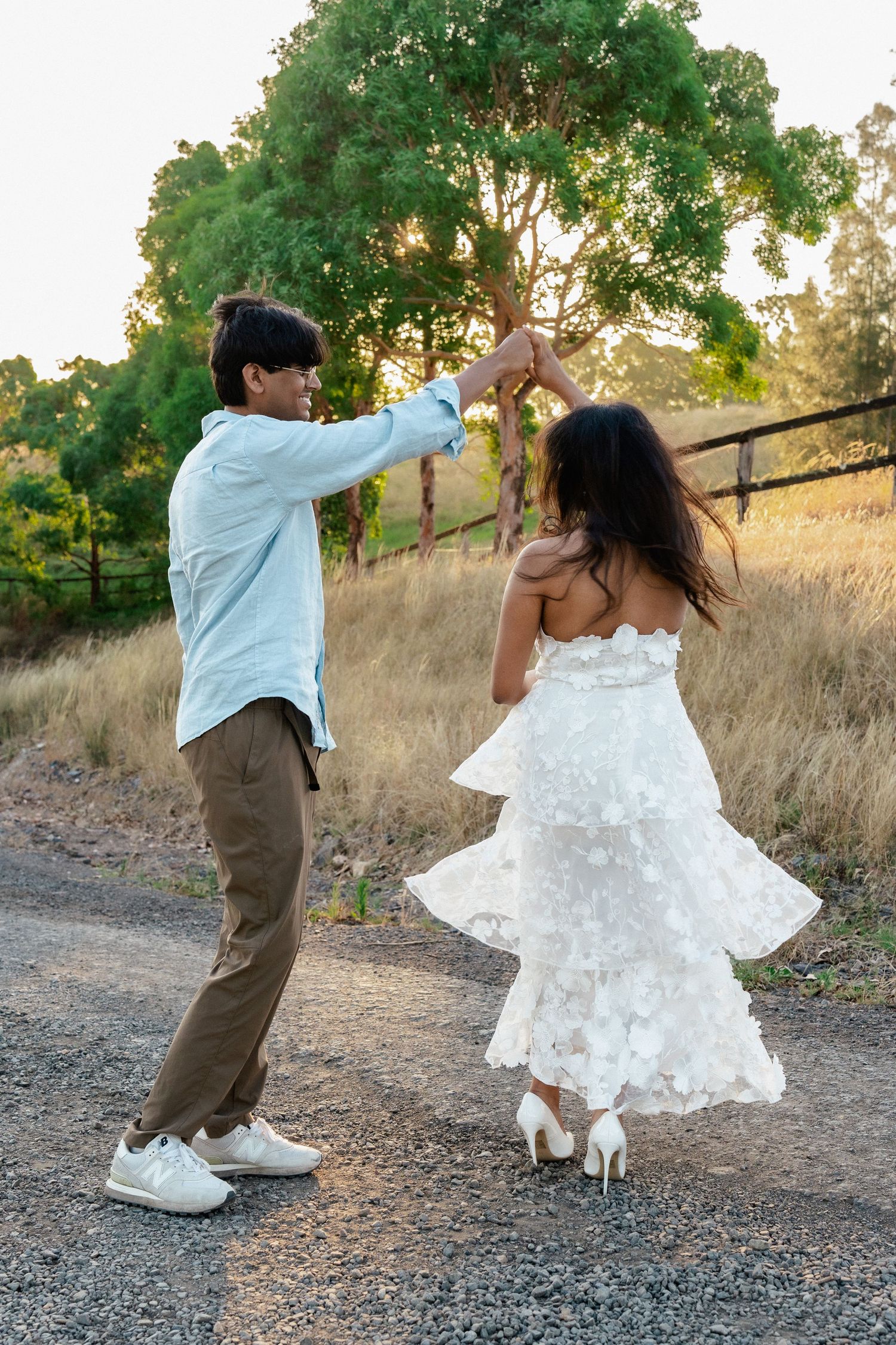 Couple dancing and twirling on a dirt path with trees and dry grass in the background.