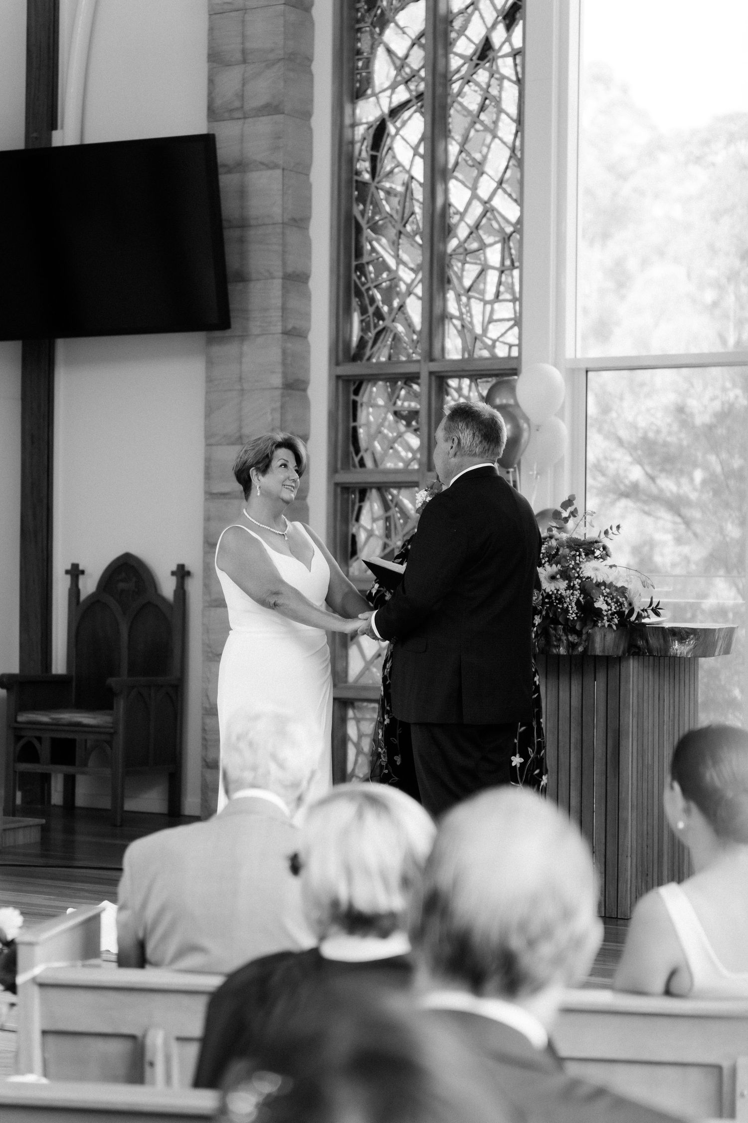 Church ceremony with guests seated in wooden pews watching proceedings at altar.