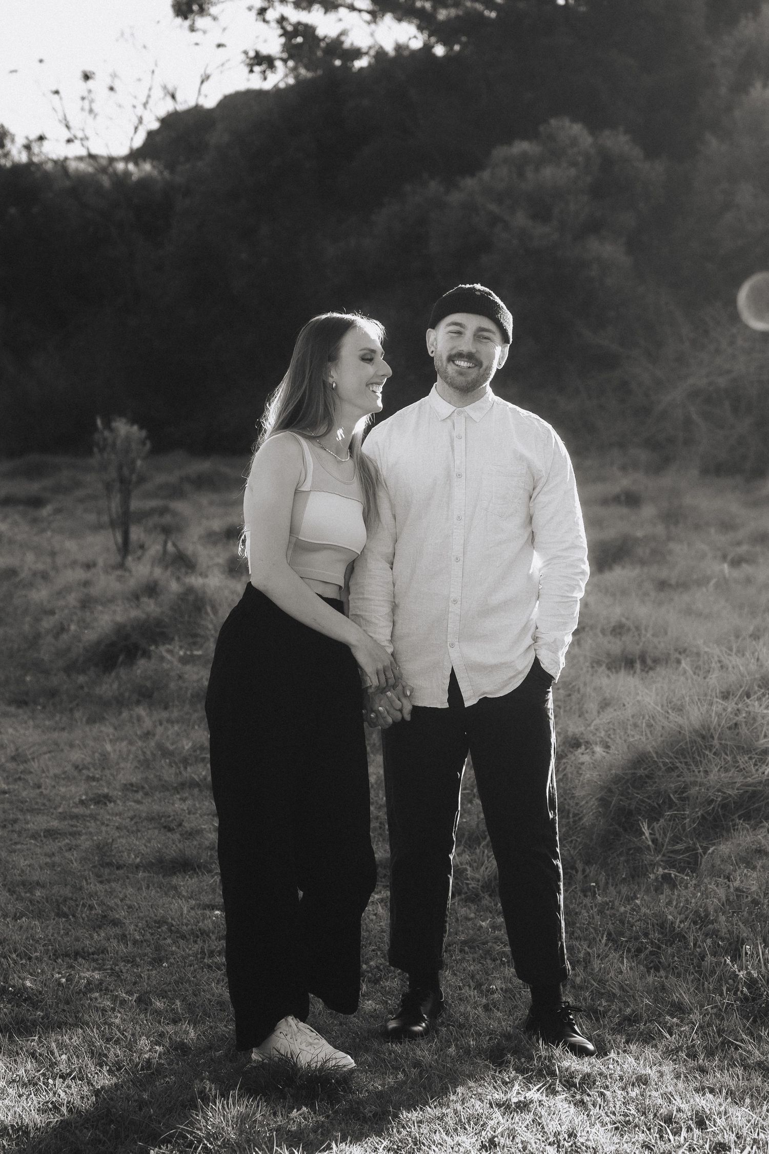 A romantic black and white photo of a couple embracing in a grassy field at sunset.
