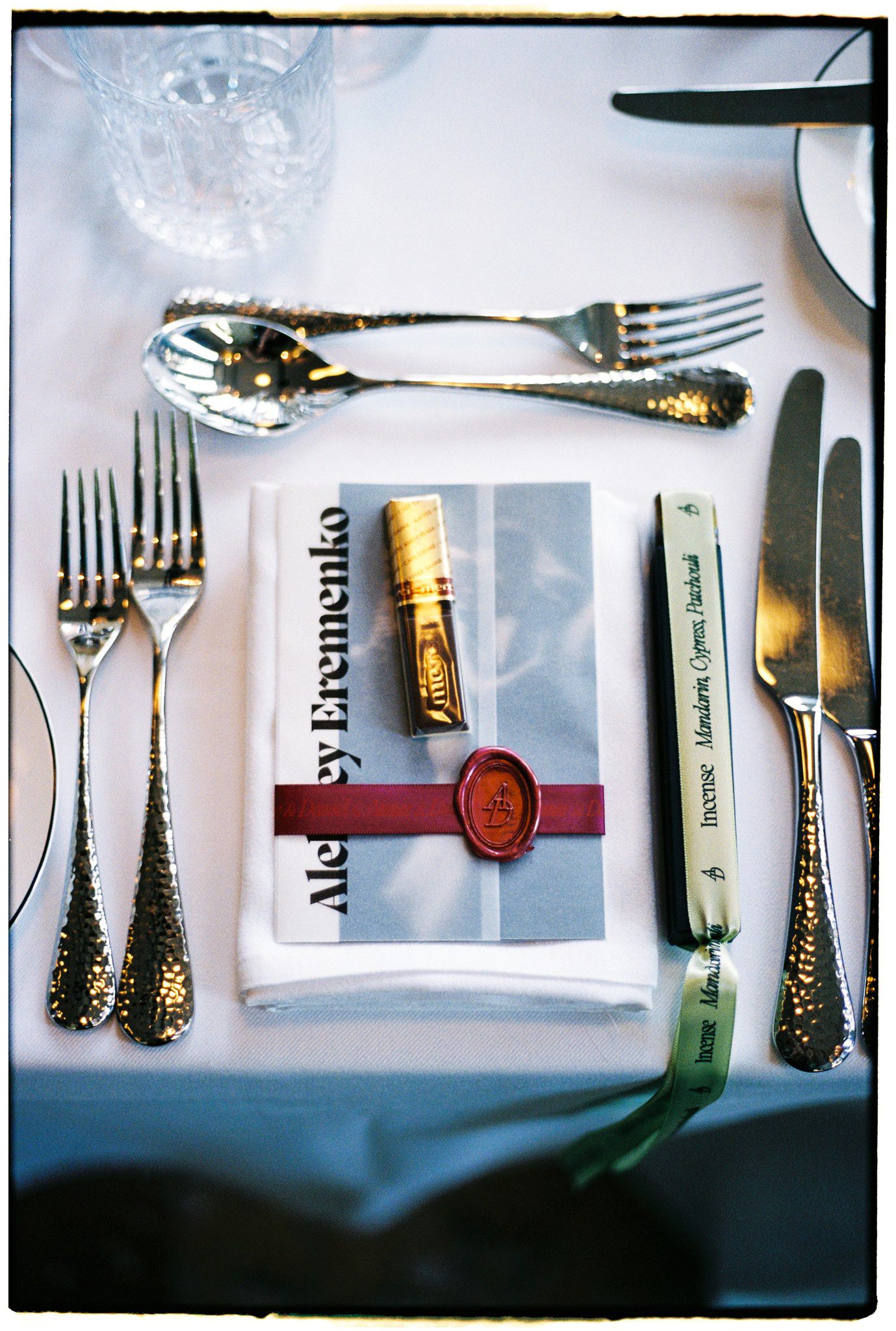Elegant place setting with silverware, wax-sealed menu card, and ribbon-tied knife on white tablecloth.