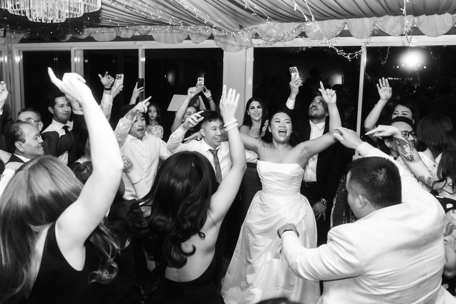 Wedding reception dance party with guests raising hands in celebration.
