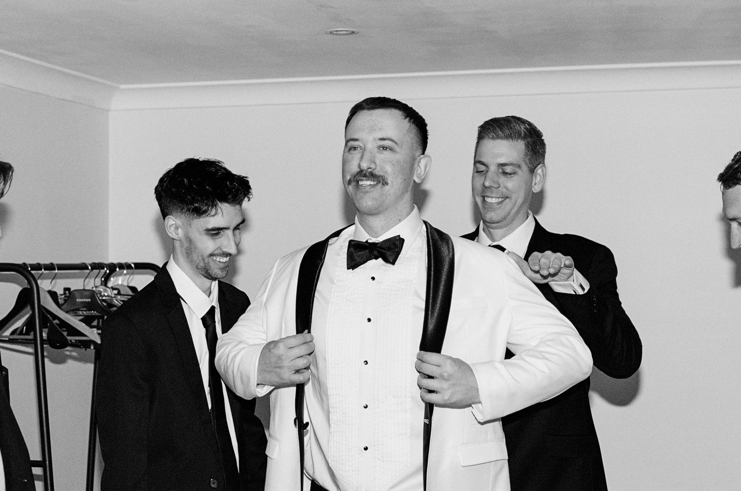 Groomsmen in formal black tuxedos and bow ties getting ready for a wedding celebration.