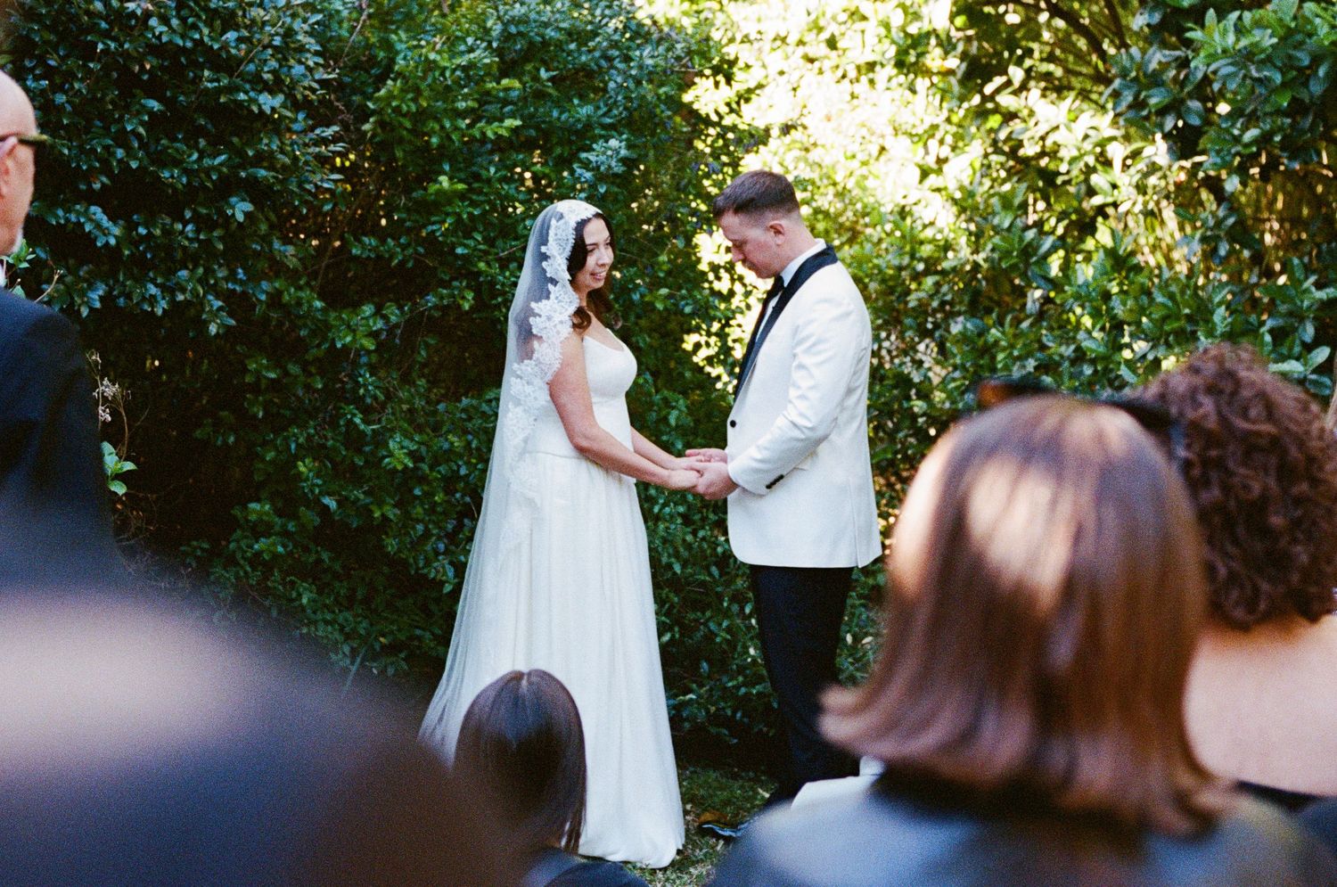 A wedding ceremony scene viewed through foliage with guests in attendance.