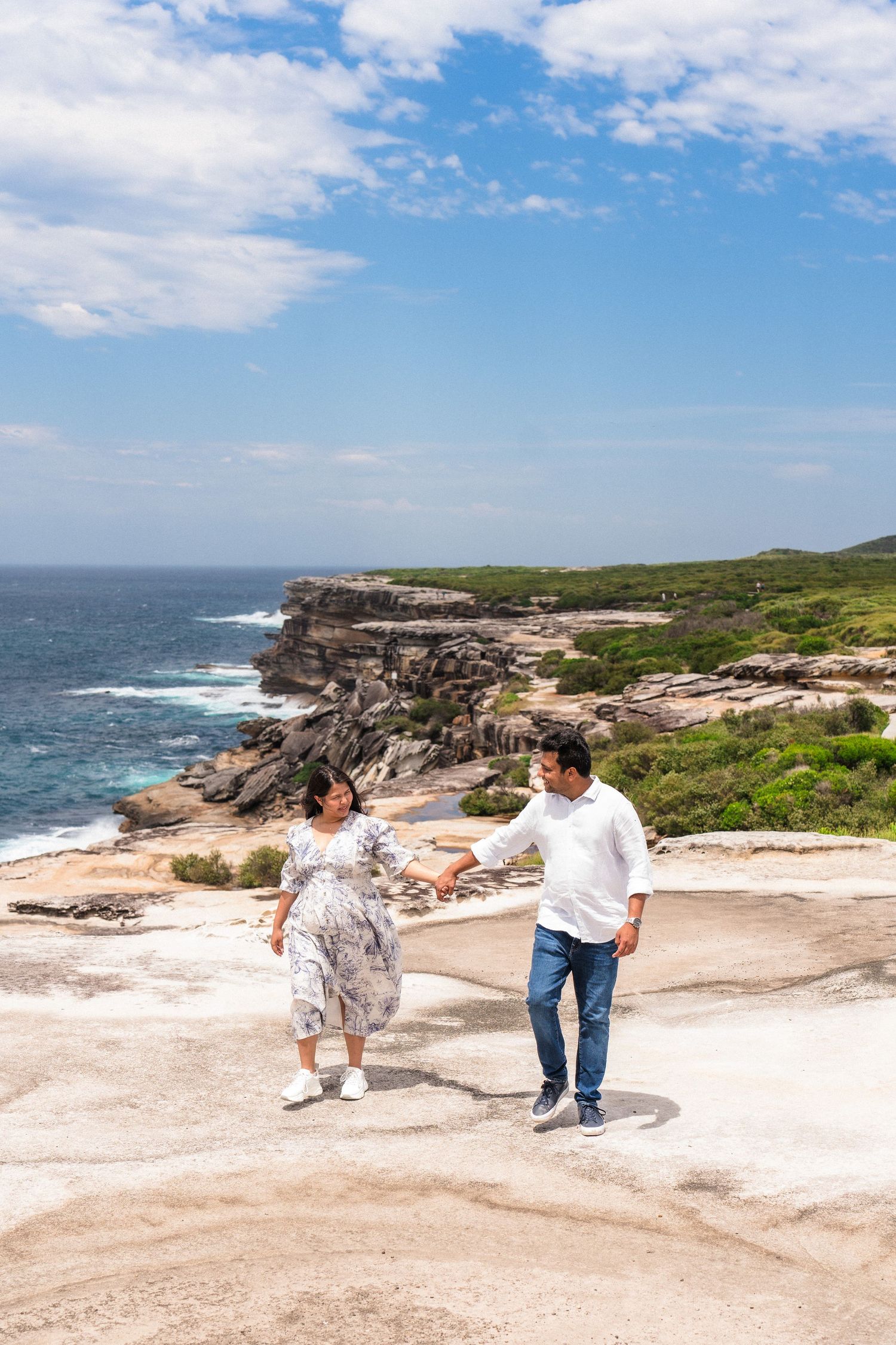 Couple dances and plays on scenic coastal rock formations by the ocean.