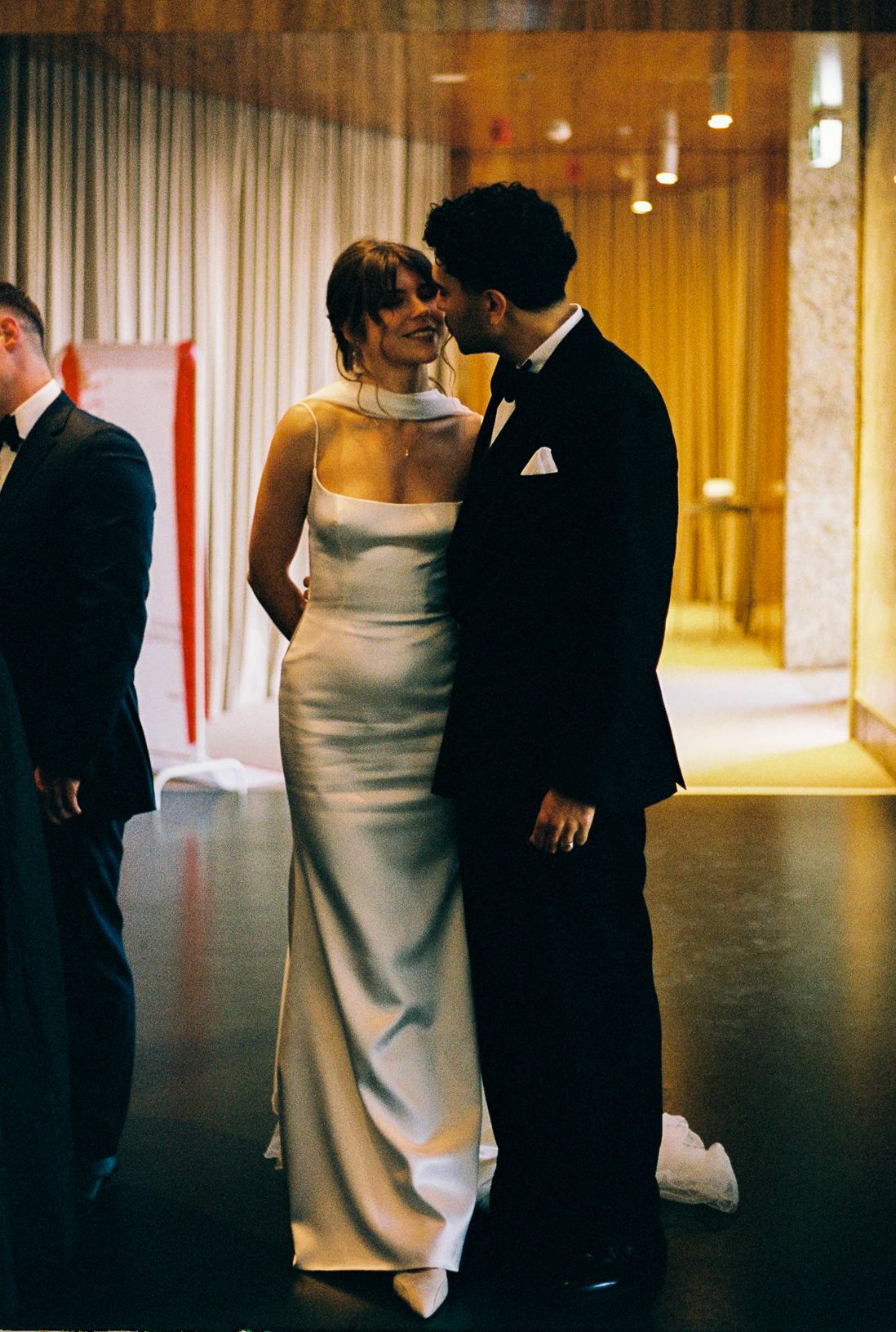 Couple in elegant formalwear sharing an intimate moment, bride in white satin gown and groom in black tuxedo.