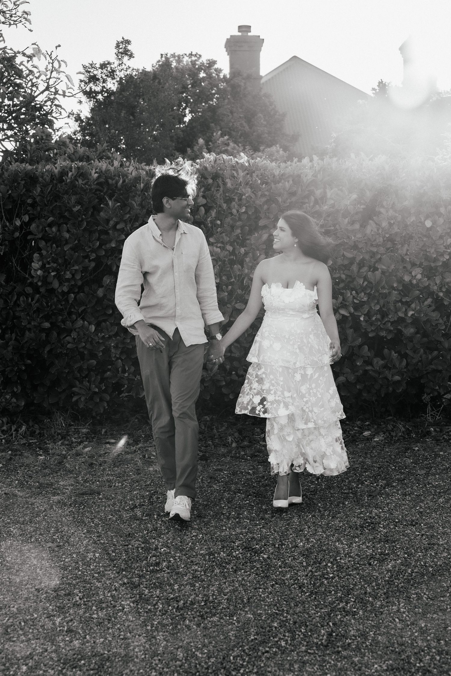A romantic black and white photo of a couple walking through a garden.