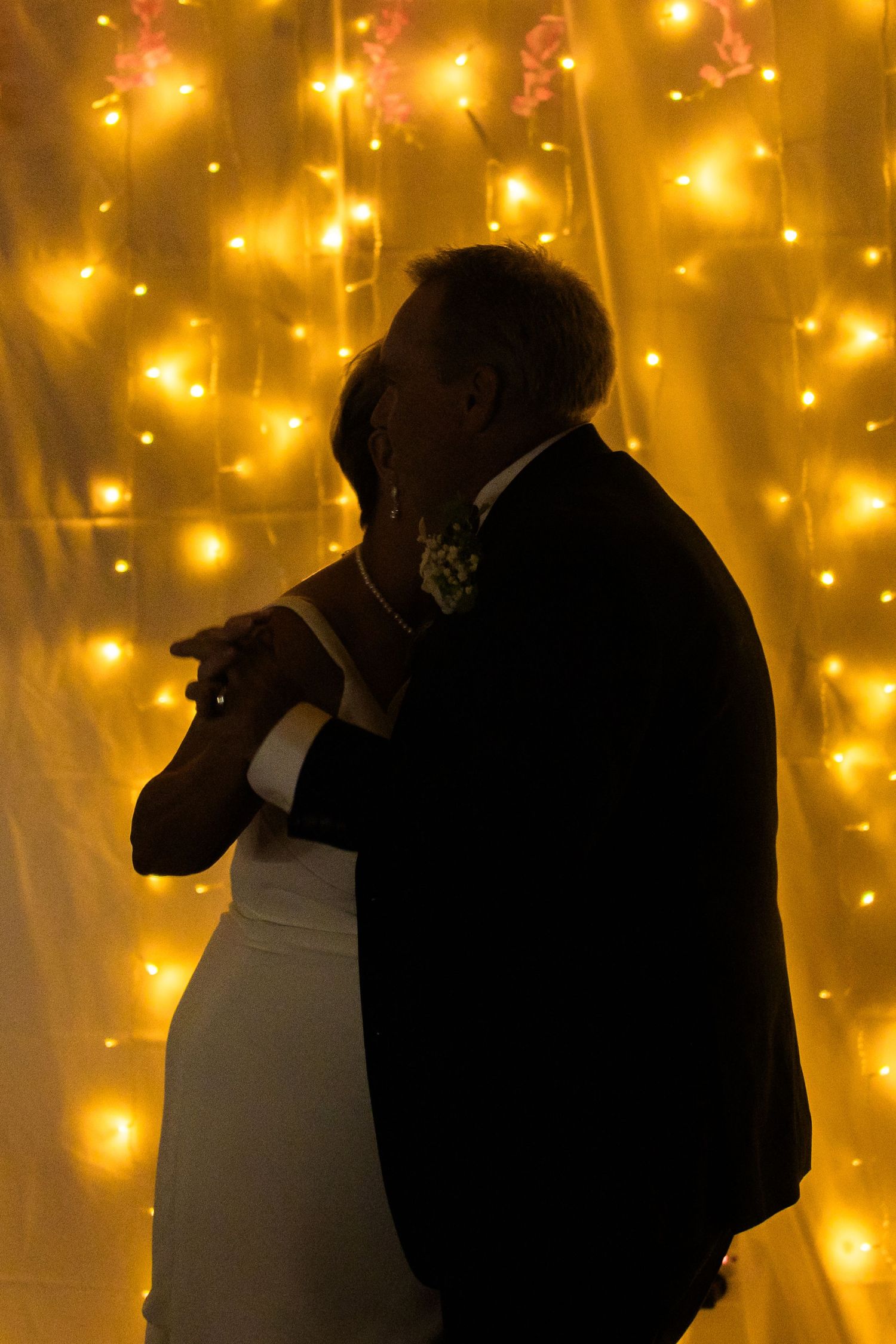 Silhouetted couple dancing against a backdrop of warm glowing string lights creating a romantic atmosphere.