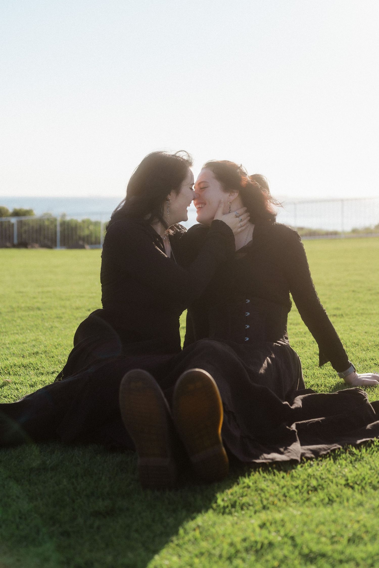 A couple in dark clothing shares an intimate moment on grass during golden hour.