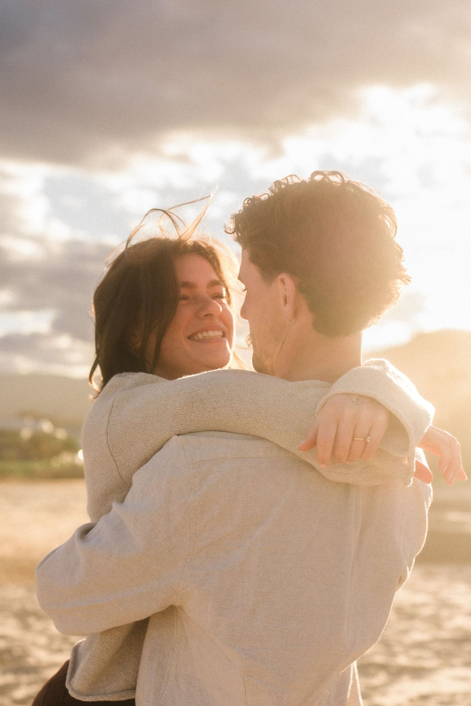 Couple embracing on beach during golden hour with dramatic sky in background.