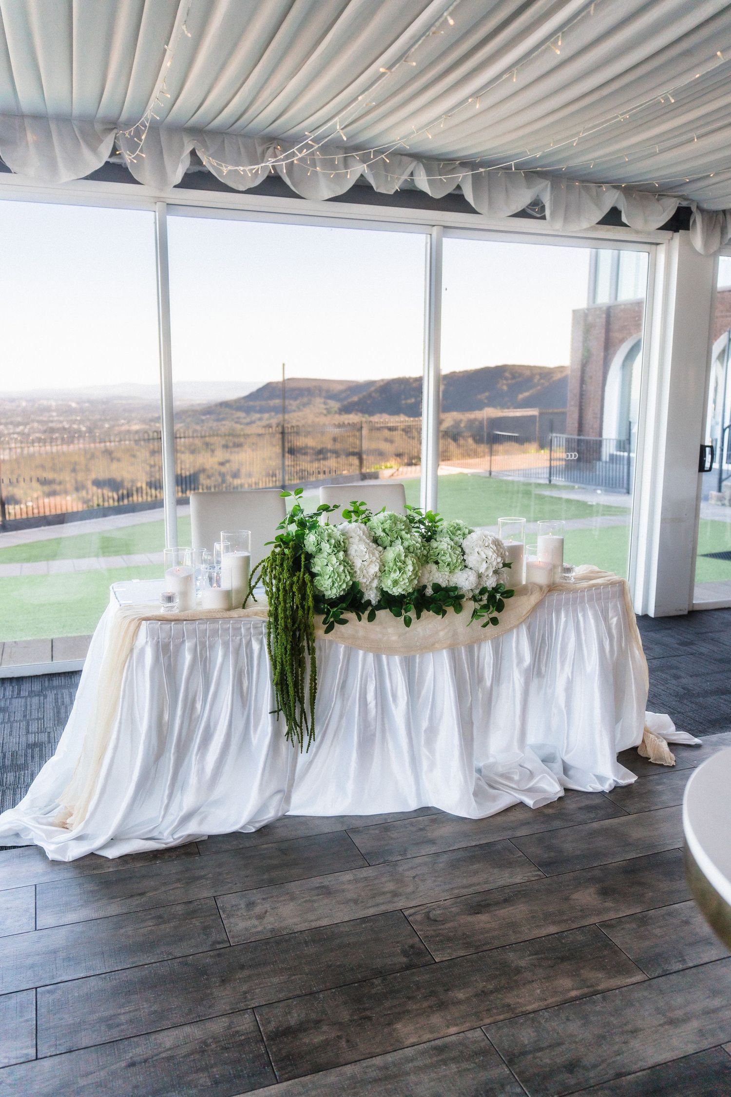 White draped buffet tables with floral arrangements in modern event space with panoramic mountain views.