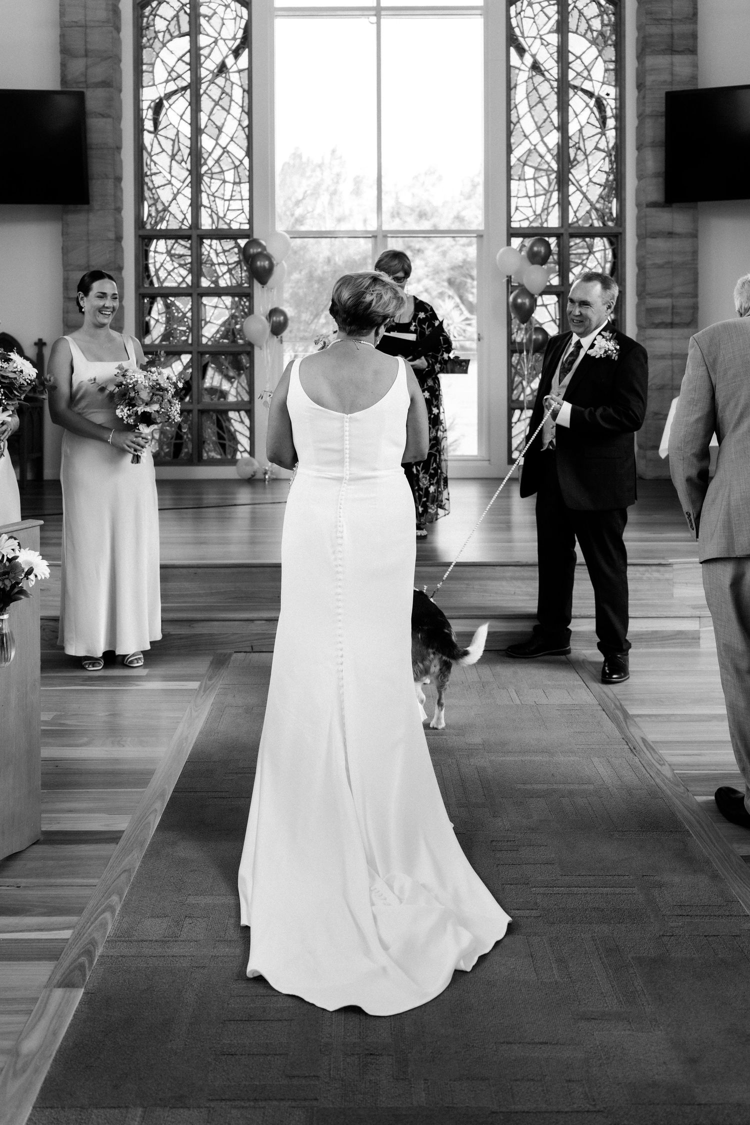 Black and white photo of wedding ceremony in church with stained glass windows.